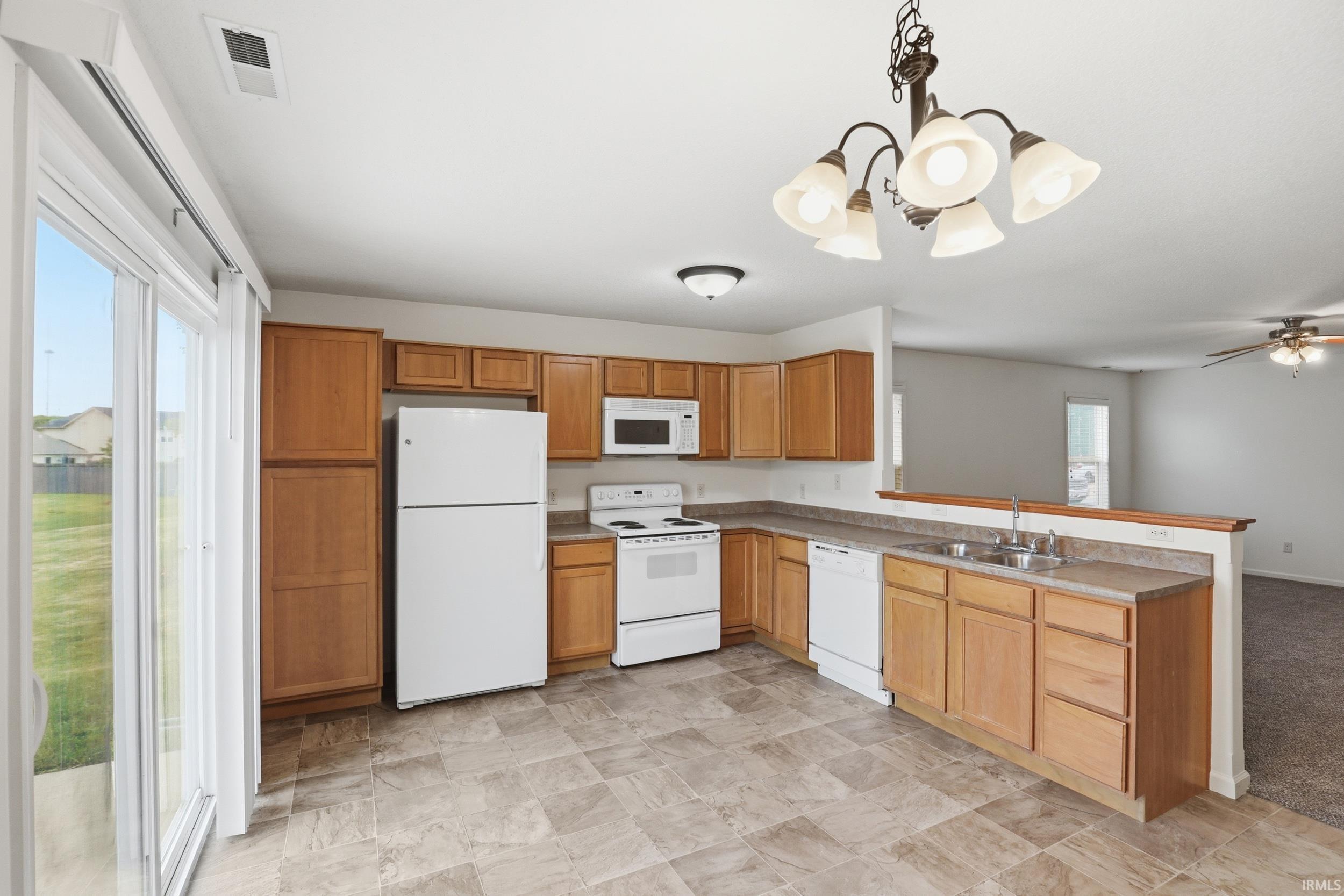 L-shaped kitchen with wood cabinetry, light-toned countertops, and white appliances