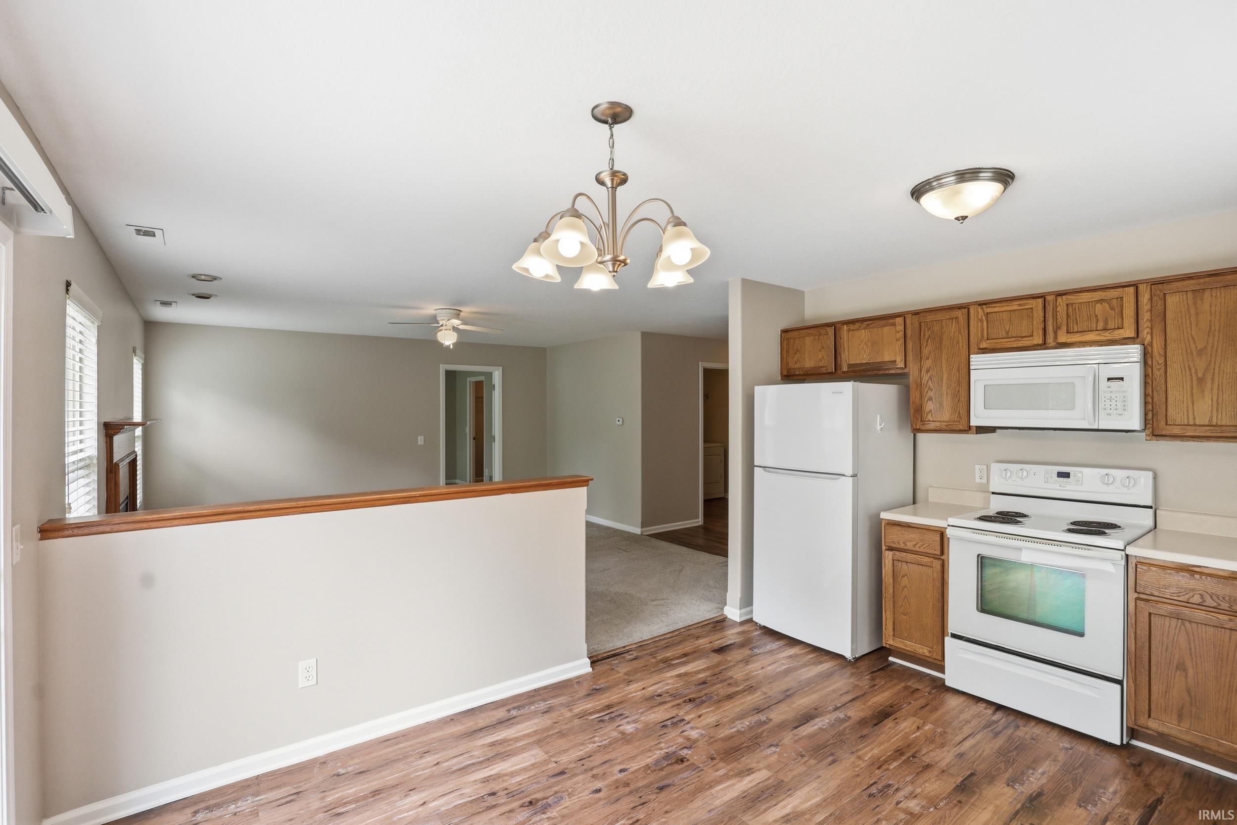 Kitchen featuring wood-finish flooring, white appliances, and warm wood cabinetry