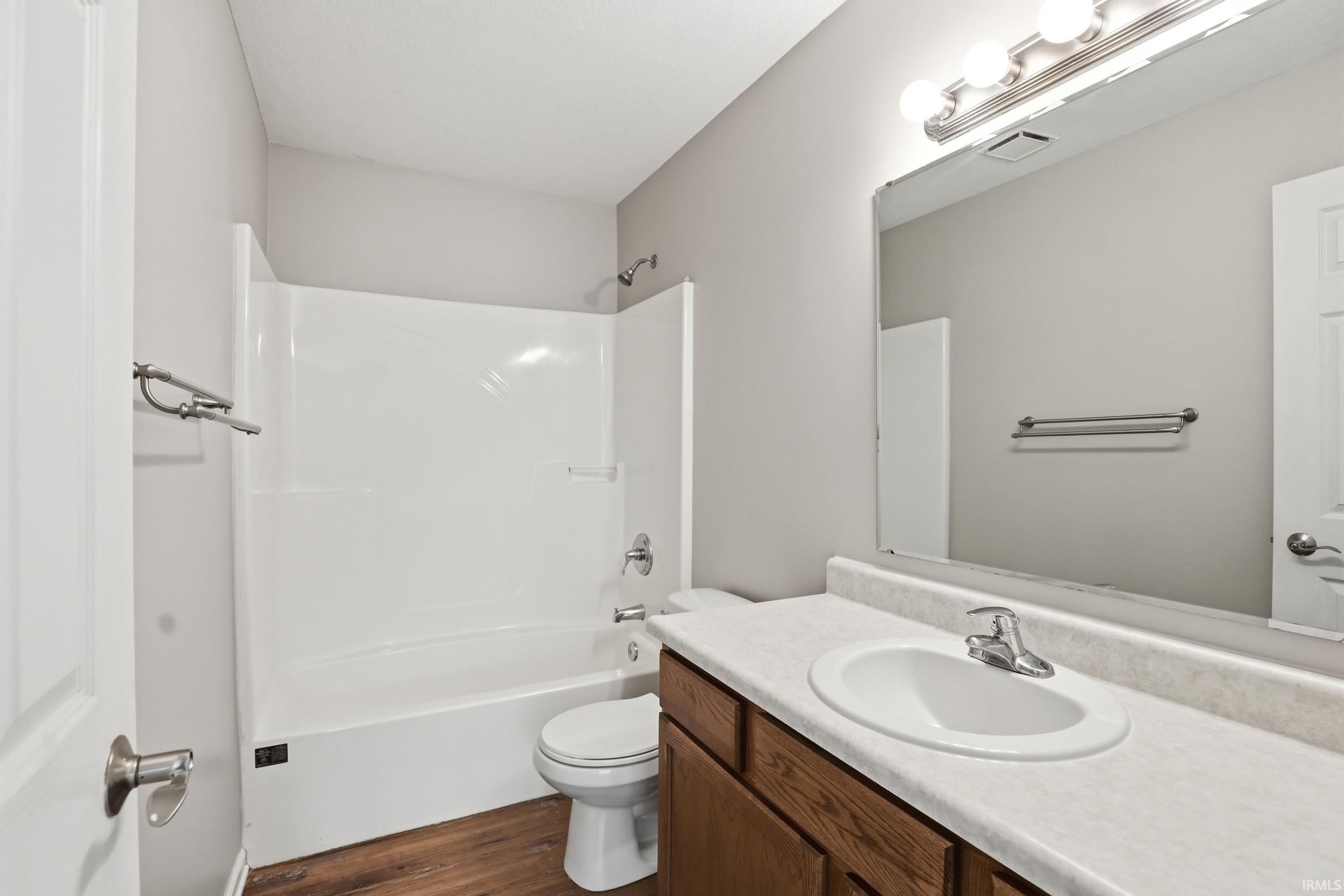 Bathroom featuring a white tub/shower combination, vanity with a white countertop and integrated sink, chrome faucet, and wood-finish flooring