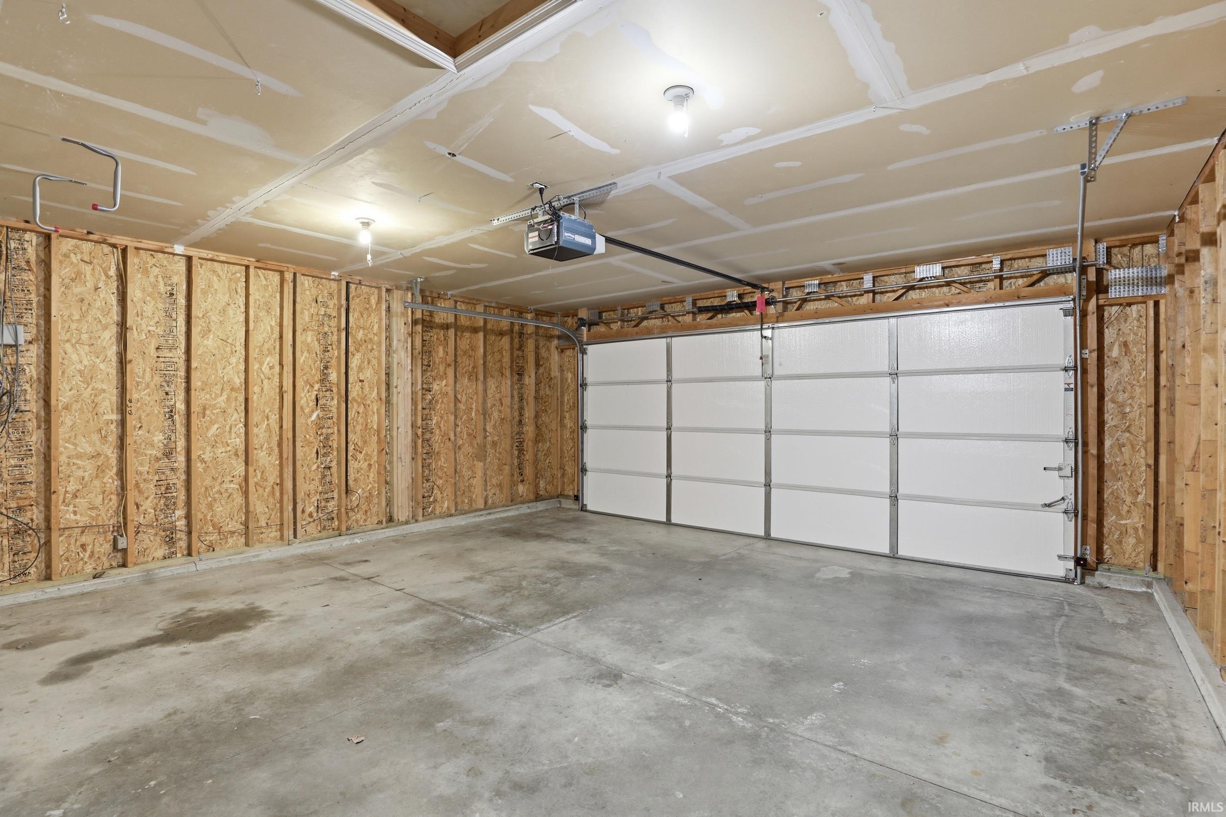 Spacious garage featuring a concrete floor, exposed wood framing, and a white paneled garage door