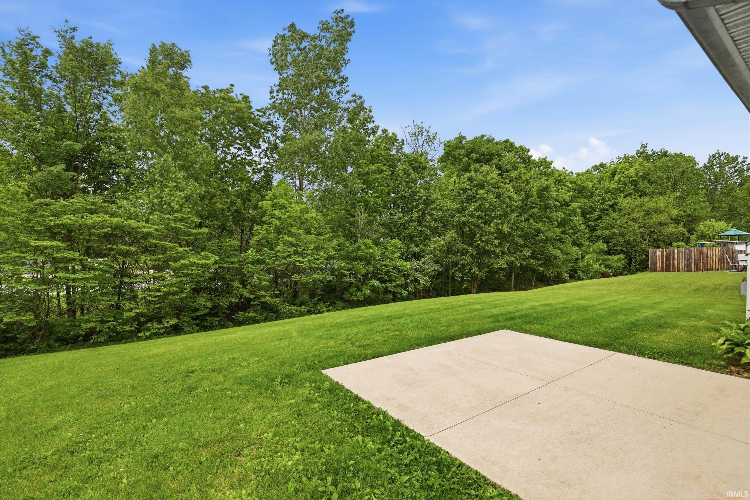 Expansive rear yard featuring a concrete patio, a lush lawn, and mature perimeter trees