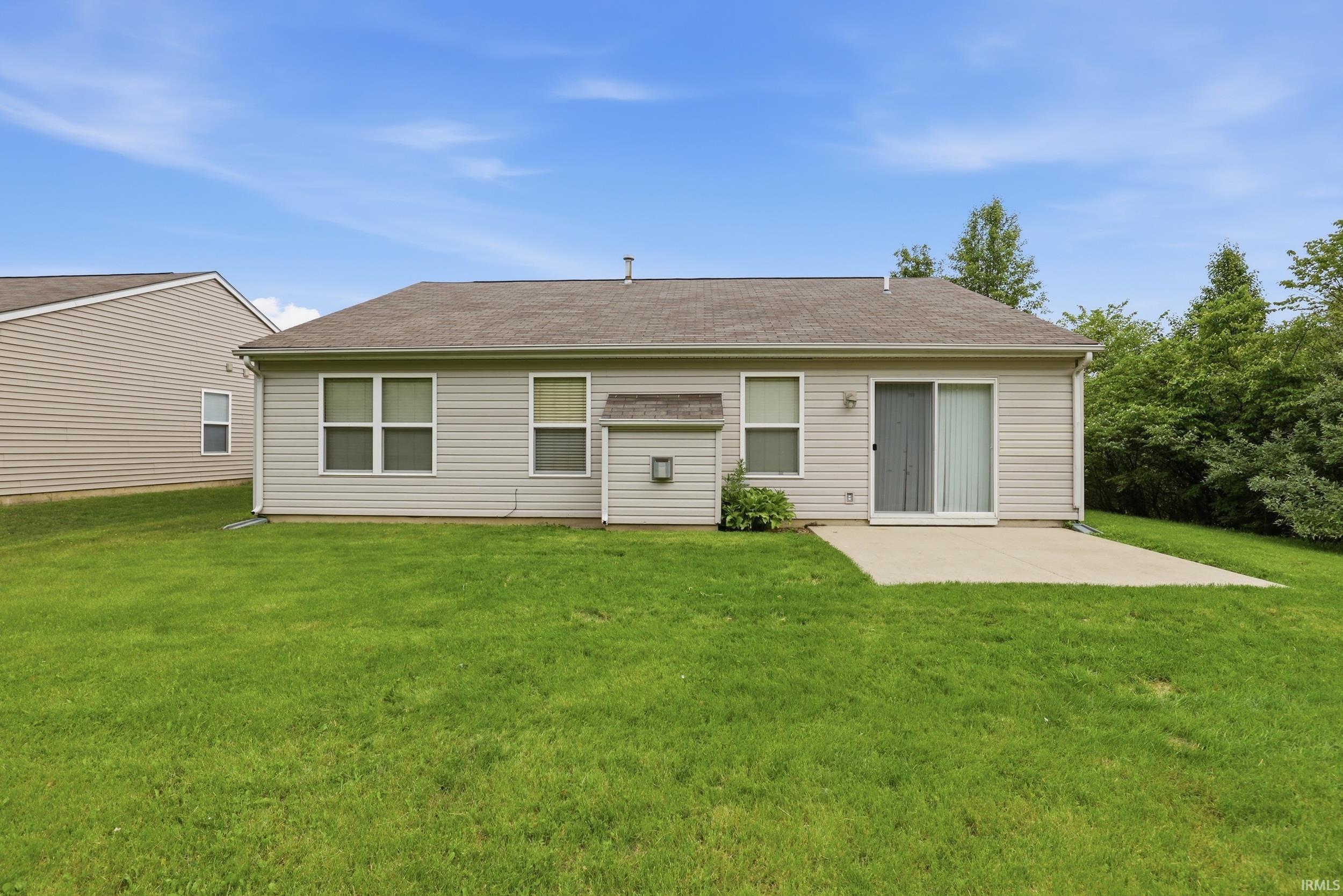 Expansive rear yard featuring a concrete patio, sliding glass door, and neutral-toned horizontal siding