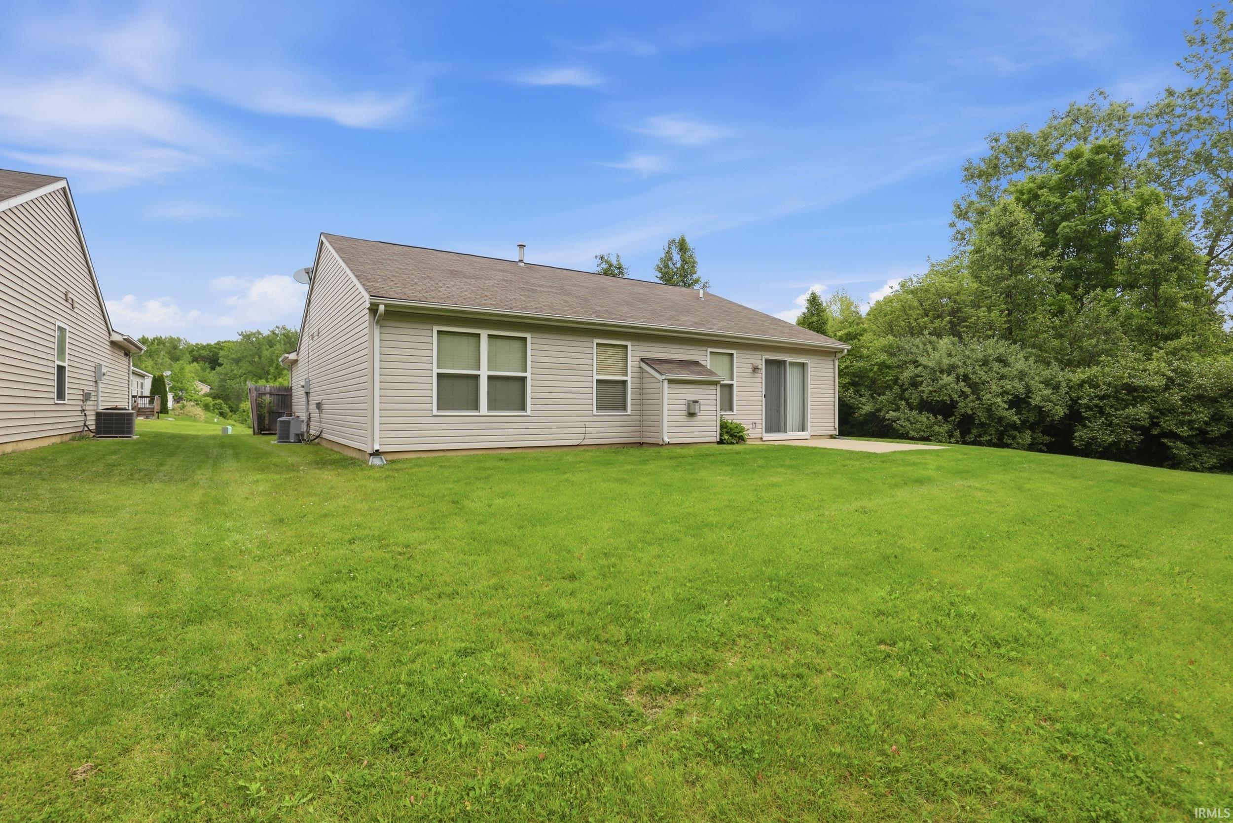 Expansive green lawn surrounds the property, featuring a concrete patio and sliding glass doors