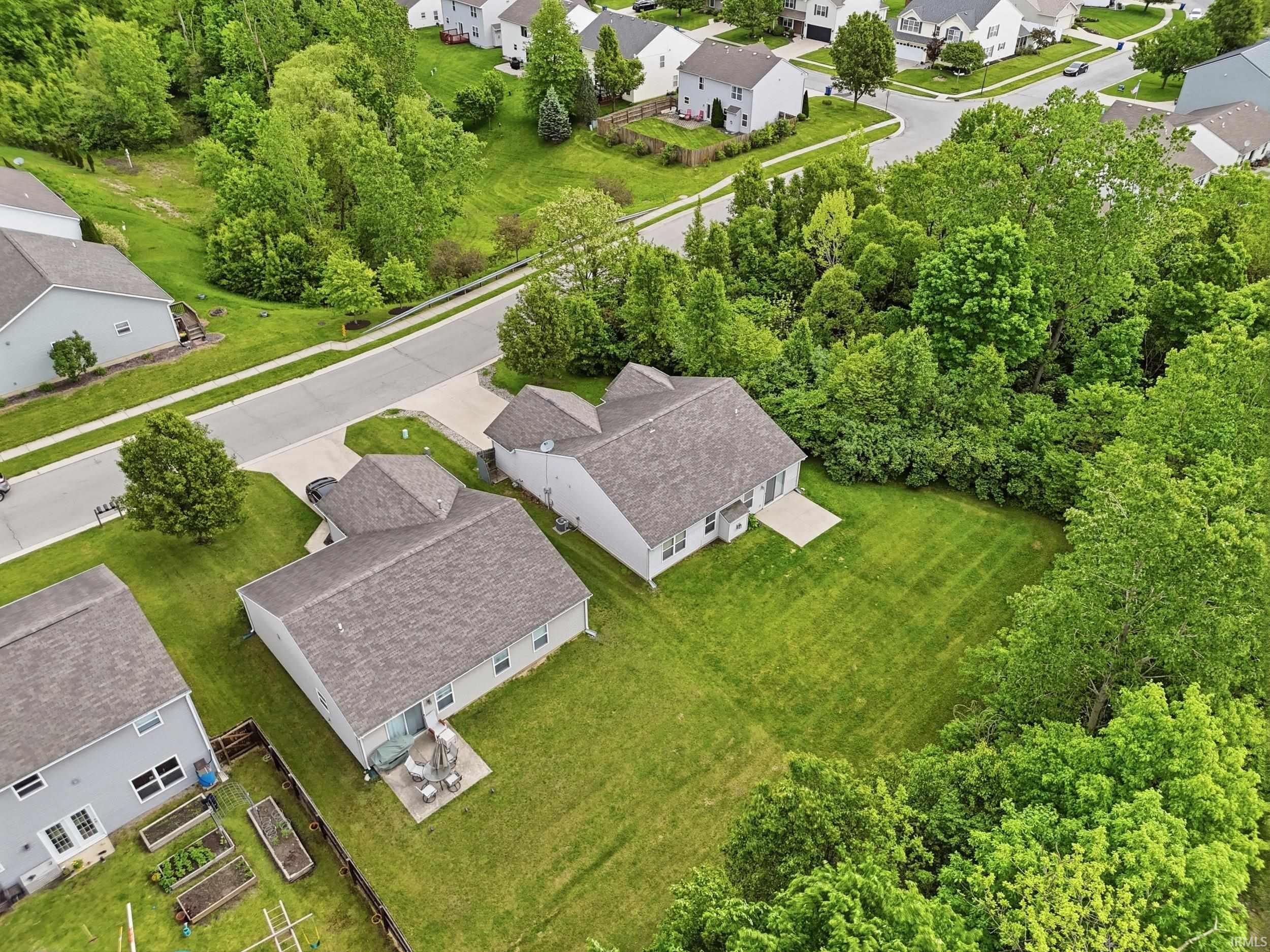 Expansive residential property featuring a large green lawn, a concrete patio, and mature trees bordering the perimeter