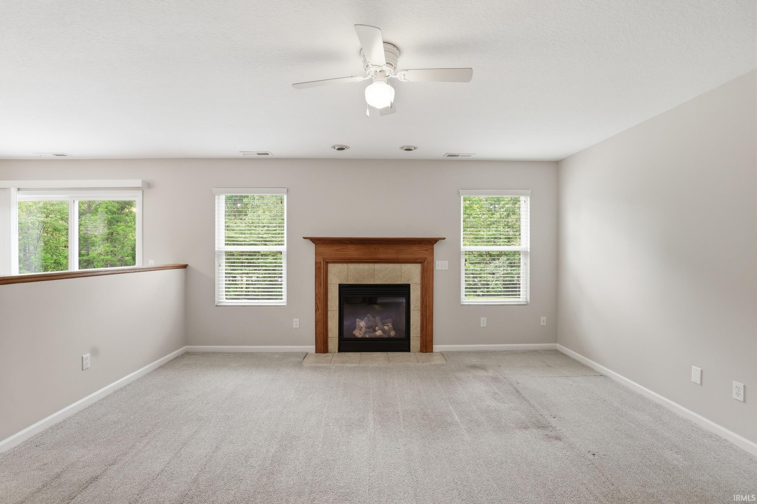 Living space featuring a fireplace with a wood-finish mantel and stone surround, light gray carpeting, and multiple windows