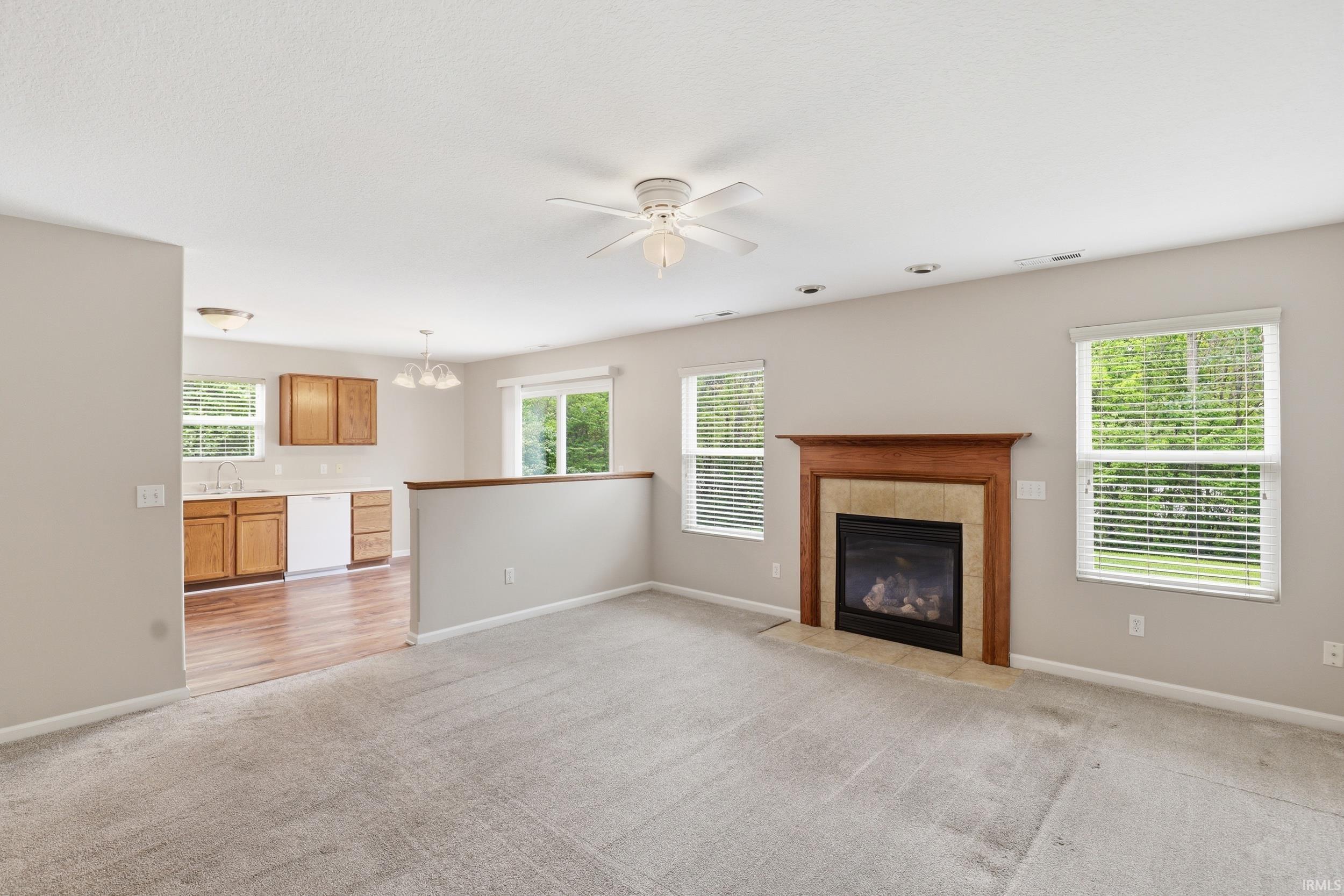Living area featuring a fireplace with a wood mantle and stone surround, neutral carpeting, and a ceiling fan