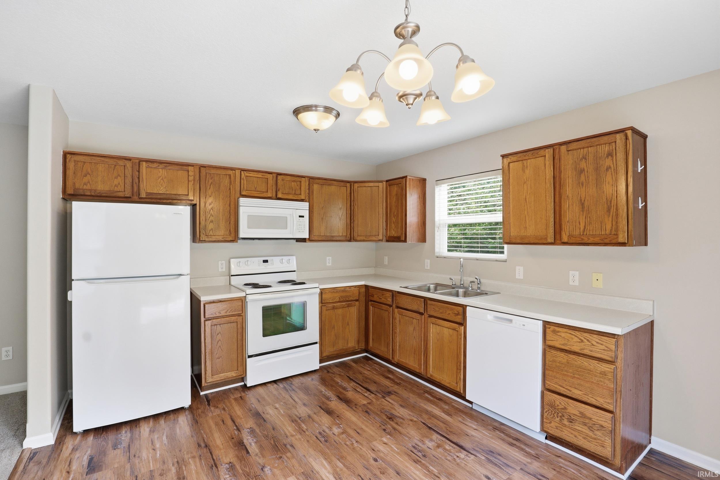 Kitchen featuring wood-finish flooring, white appliances, wood cabinetry, and a window
