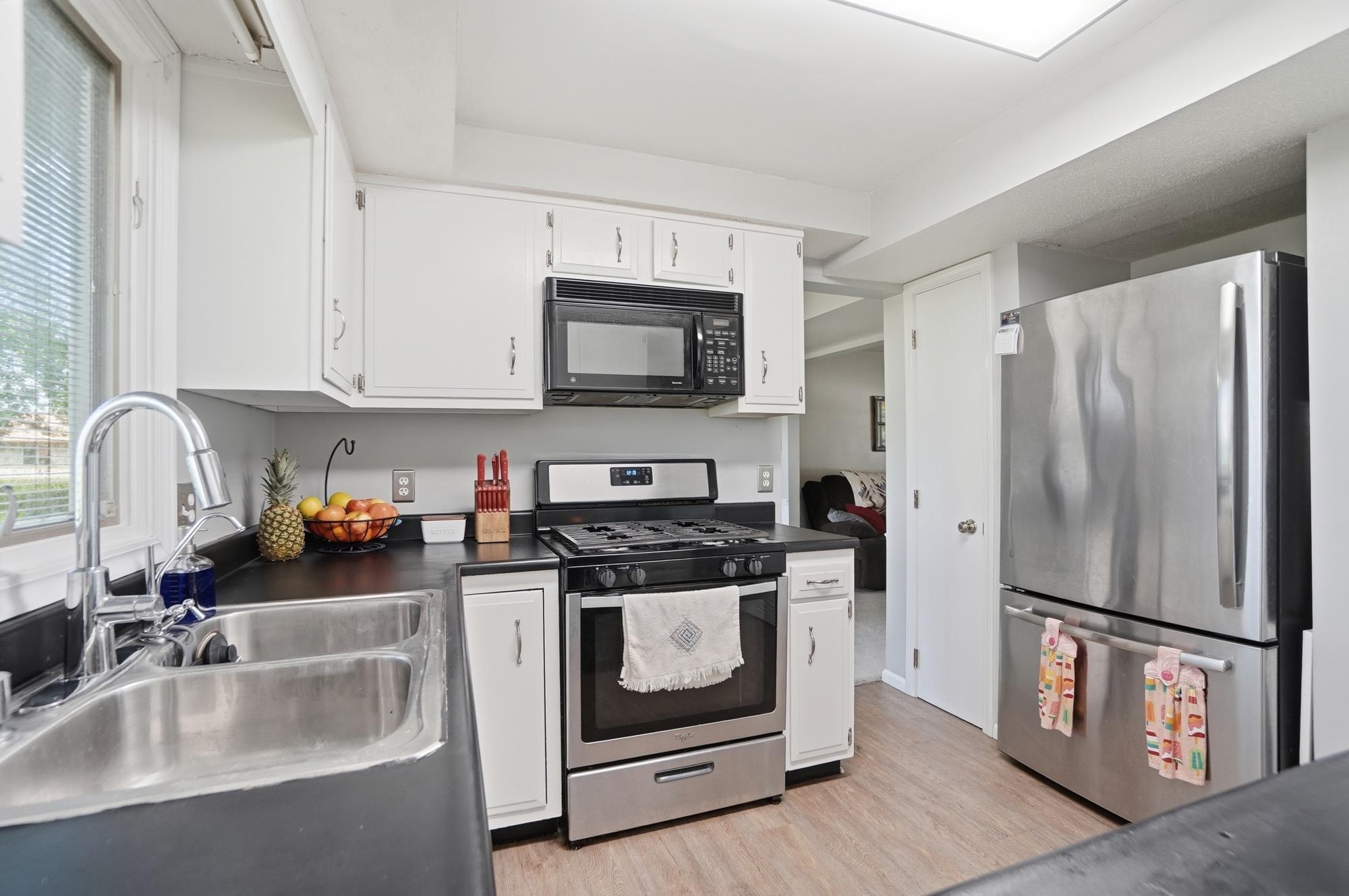 Kitchen featuring white cabinetry, dark countertops, stainless steel appliances, and wood-finish flooring