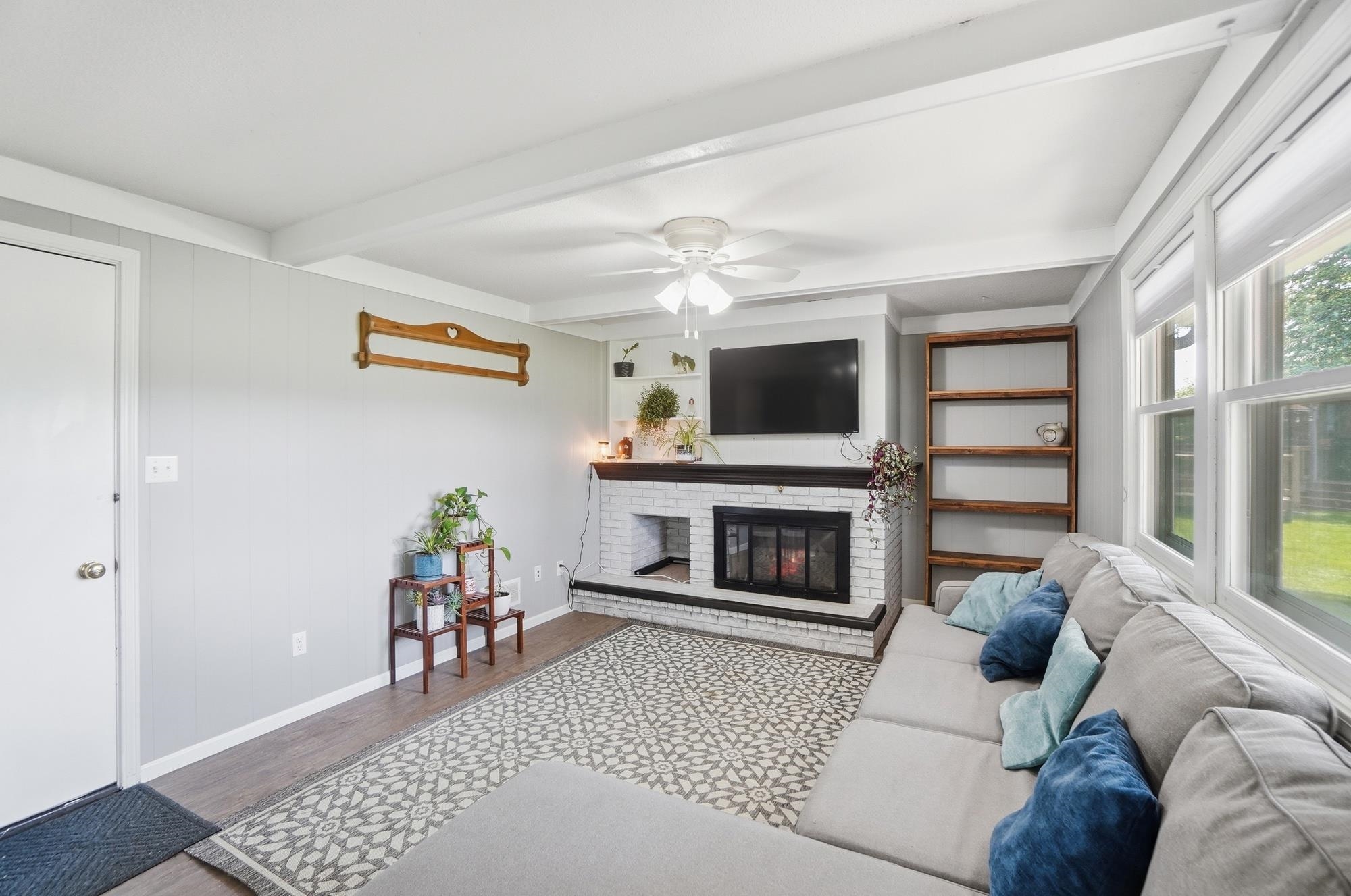 Living space featuring a whitewashed brick fireplace with a dark wood mantel, wood-finish flooring, and a ceiling fan