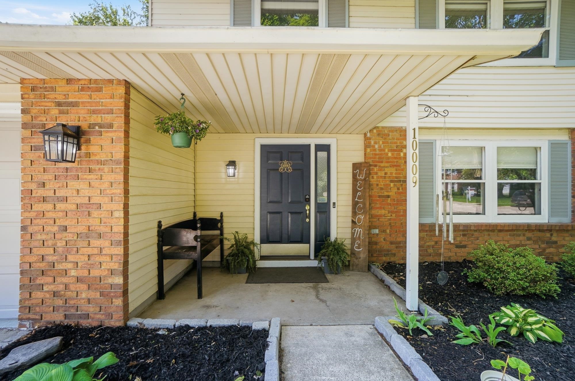 Inviting front entrance with a dark paneled door, brick column accents, and light-colored siding