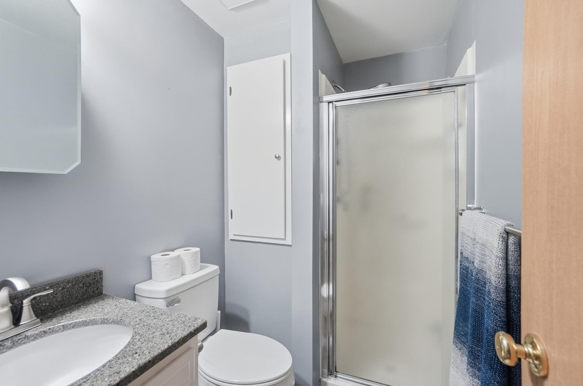 Bathroom featuring a chrome-framed shower enclosure with frosted glass, a vanity with a stone-finish countertop and undermount sink, a wall-mounted medicine cabinet, and a built-in storage cabinet