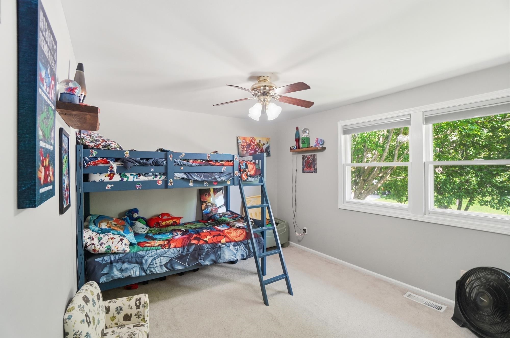 Bright room featuring dual windows with white trim, light gray walls, a ceiling fan with integrated lighting, and neutral carpeting