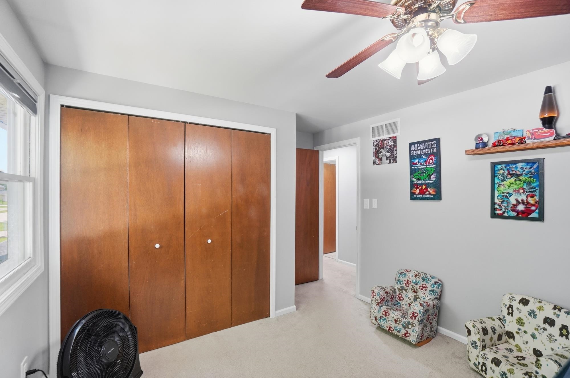 Bedroom featuring light gray walls, carpet flooring, a window with white trim, a ceiling fan with light fixture, and wood bi-fold closet doors