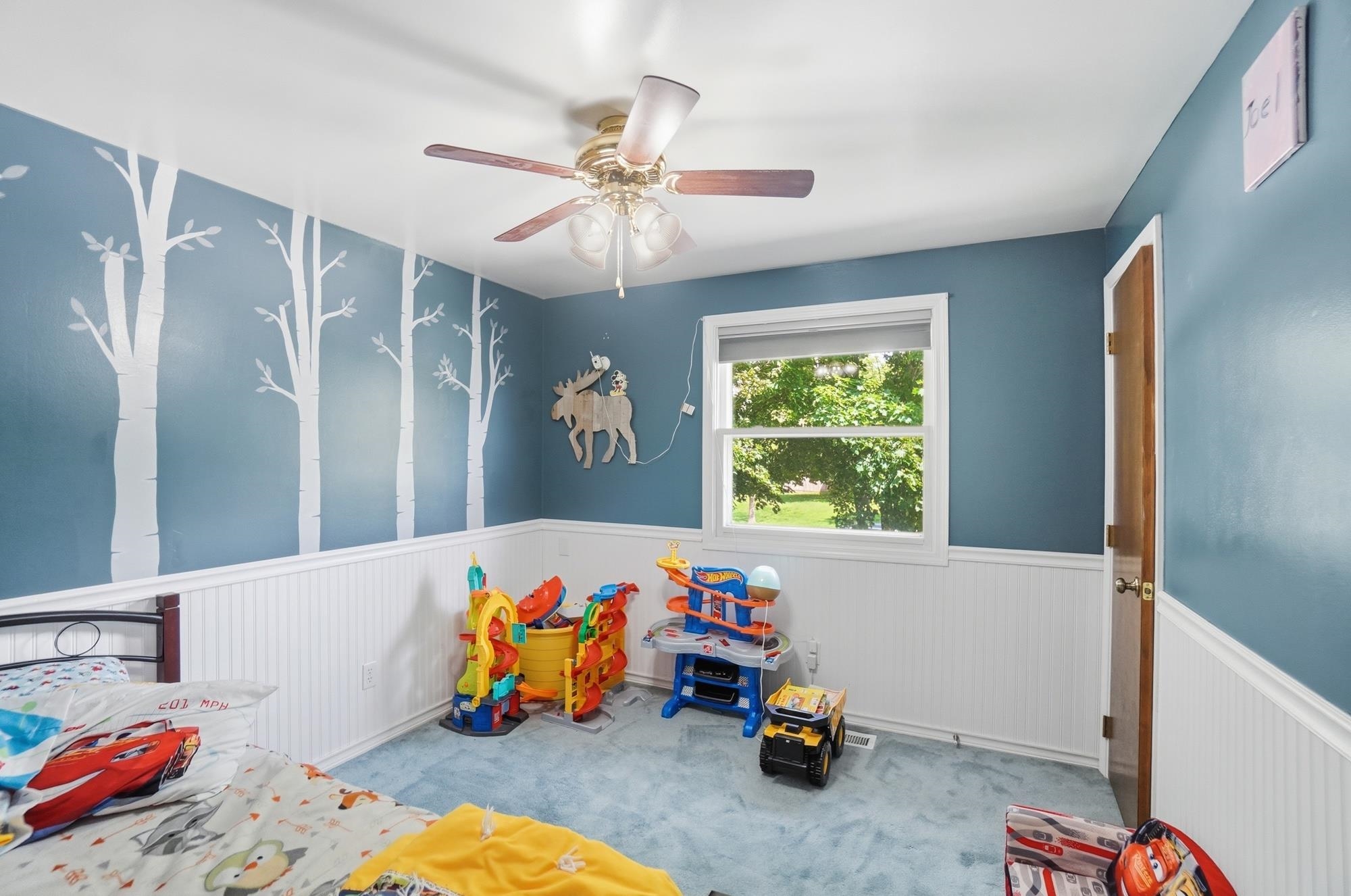 Room featuring blue walls, white wainscoting, and a ceiling fan with integrated lighting