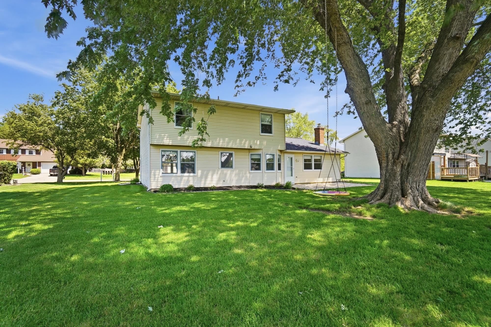 Expansive green lawn surrounds the property, featuring a two-story residence with light-colored siding and multiple windows