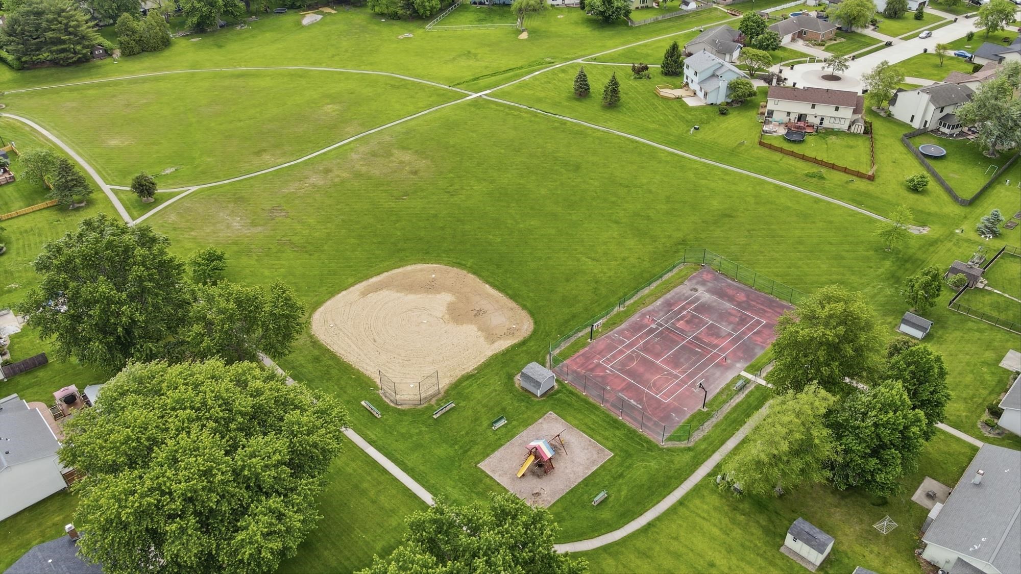 Expansive green space featuring a baseball diamond, a tennis court, a playground area, and walking paths