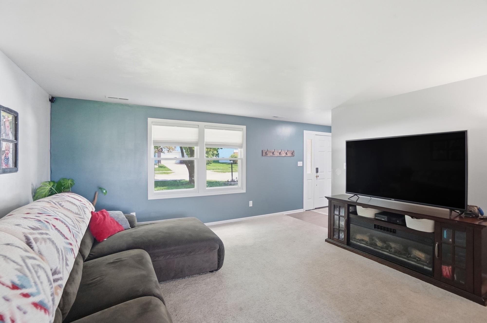 Bright living area featuring a large window, light-colored carpeting, a white entry door, and a built-in media console with an integrated electric fireplace