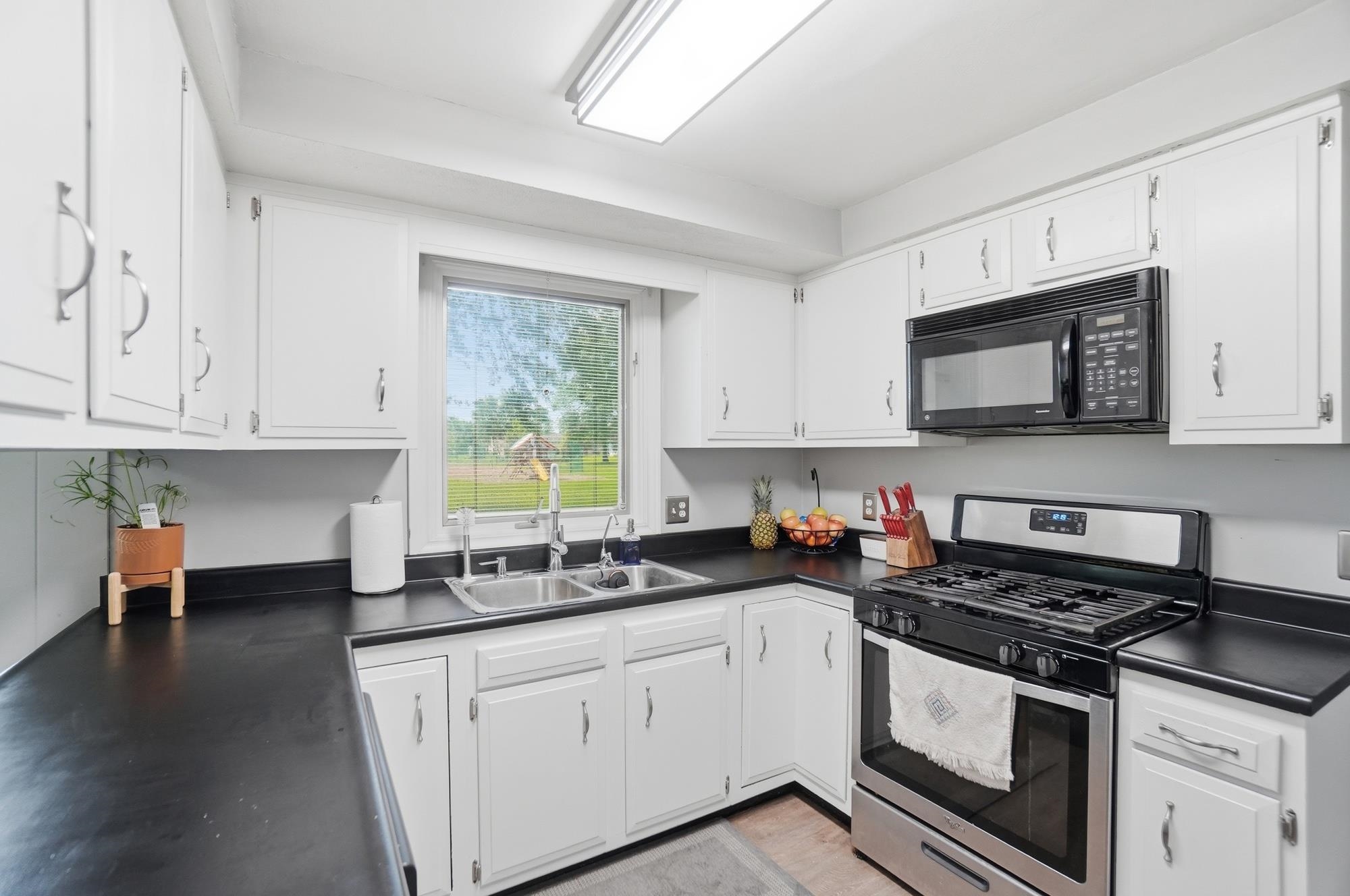 Kitchen featuring white cabinetry, dark countertops, a double basin stainless steel sink, an over-range microwave, and a stainless steel gas range