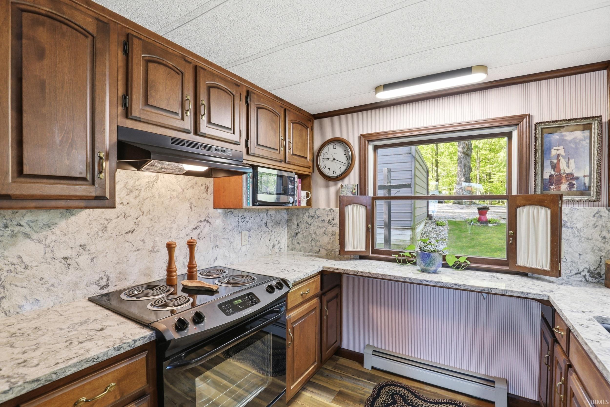 Kitchen featuring wood cabinetry, stone-finish countertops, and a black electric range with an overhead ventilation hood