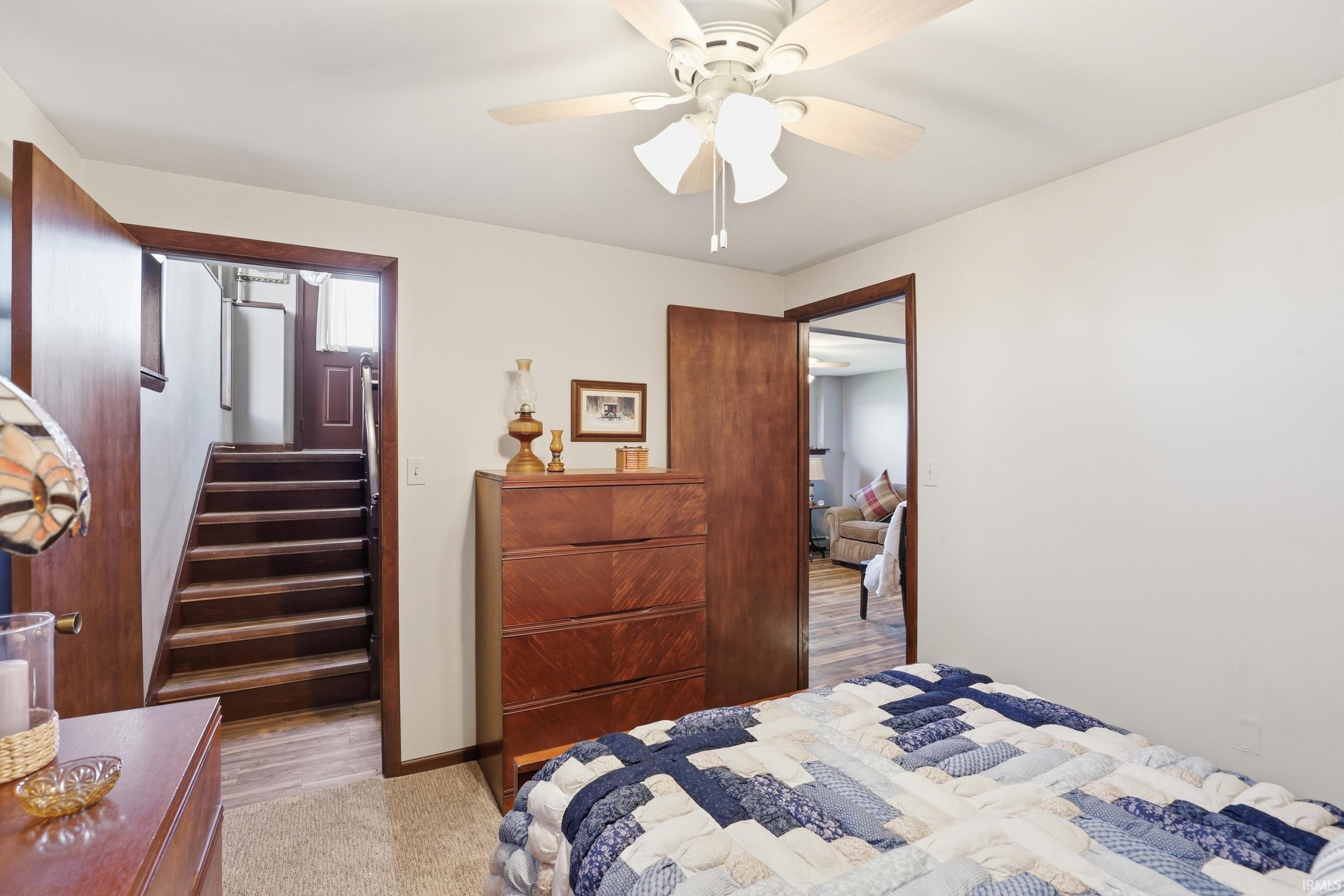 Interior room featuring a ceiling fan with light fixture, white walls, and a doorway opening to a wooden staircase
