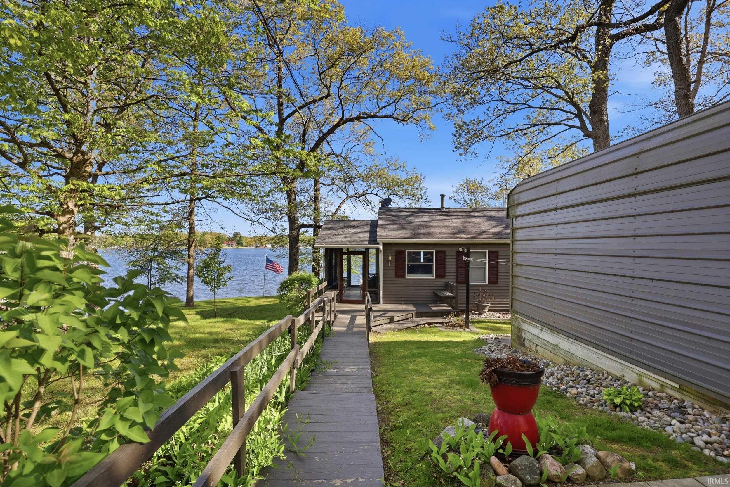 Wood-finish boardwalk leading to a waterfront property with mature trees and a metal-sided outbuilding