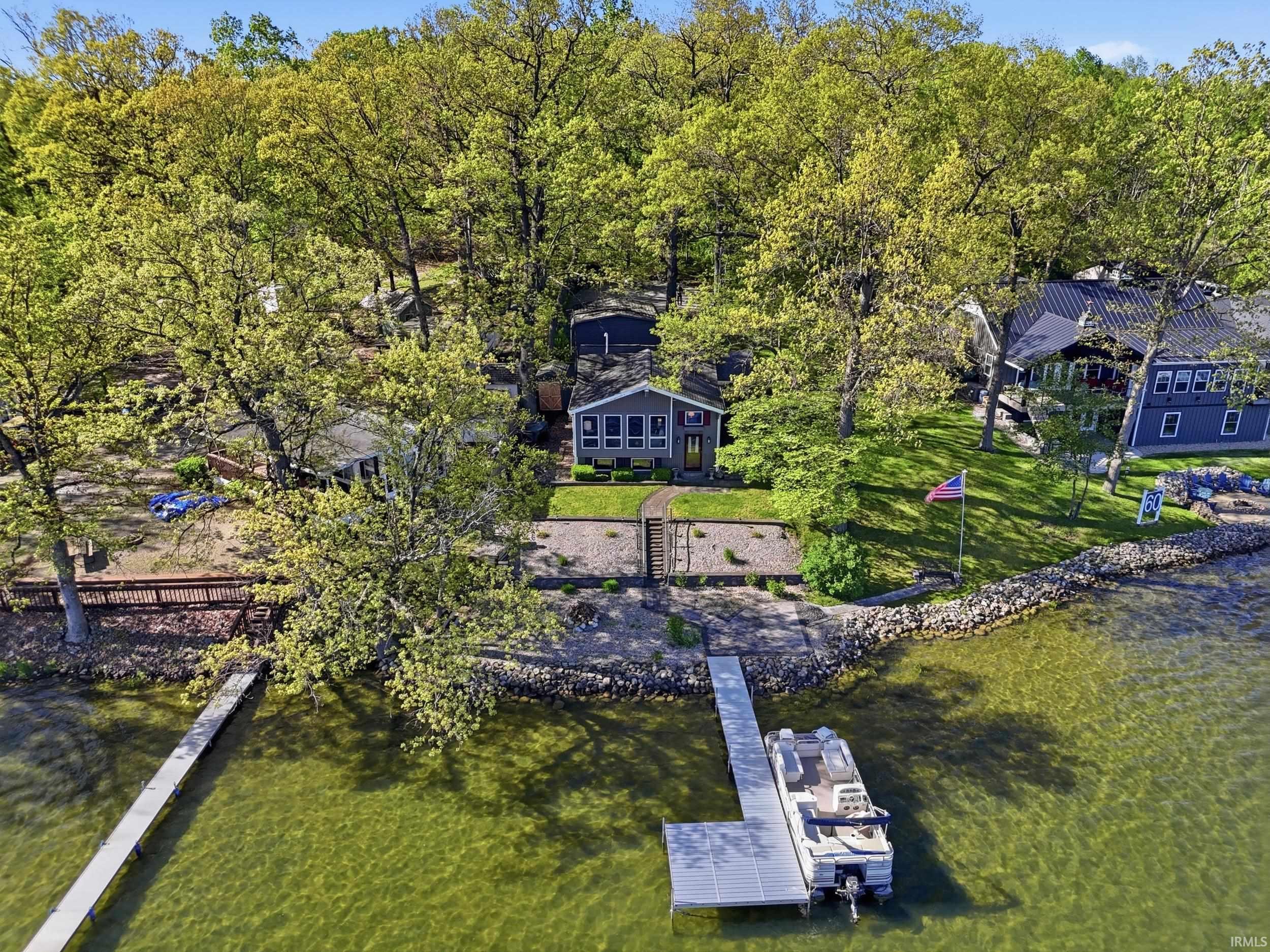 Waterfront property featuring a private boat dock, lush green landscaping, and mature trees