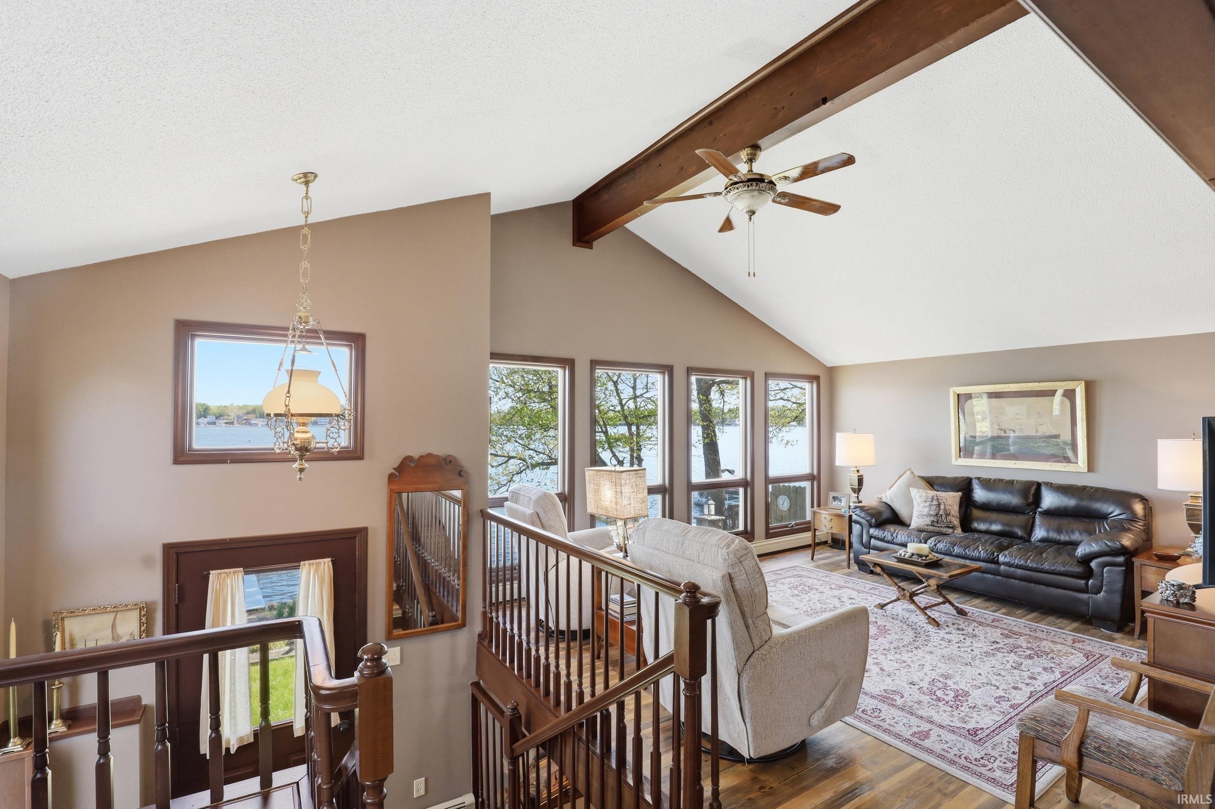 Living area featuring a vaulted ceiling with exposed wood beams, a ceiling fan, and wood-finish flooring
