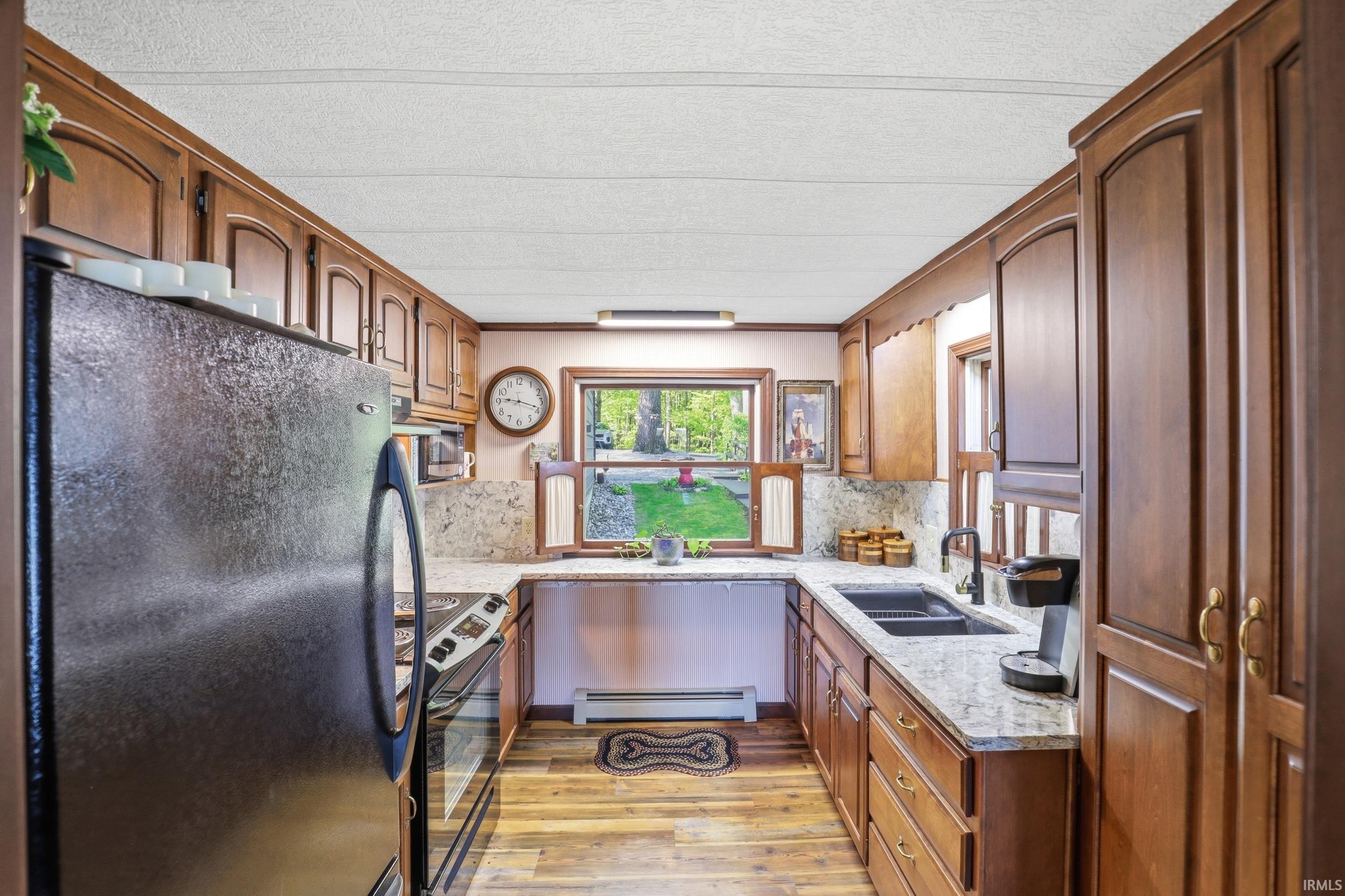 U-shaped kitchen featuring wood-finish cabinetry, granite-style countertops, wood-finish flooring, and a window above the sink