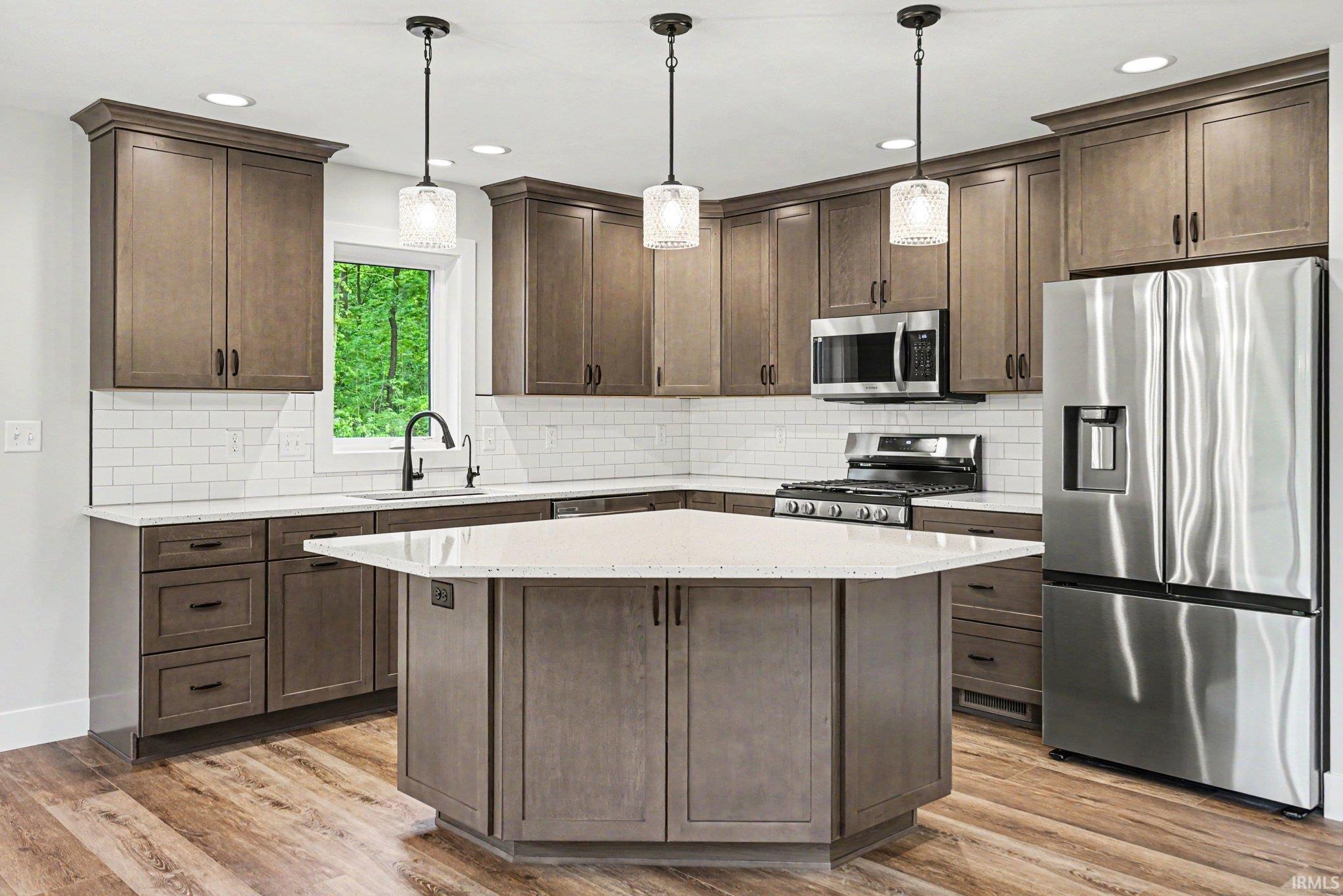 Kitchen featuring wood-finish flooring, shaker-style cabinetry, quartz countertops, a subway tile backsplash, and stainless steel appliances