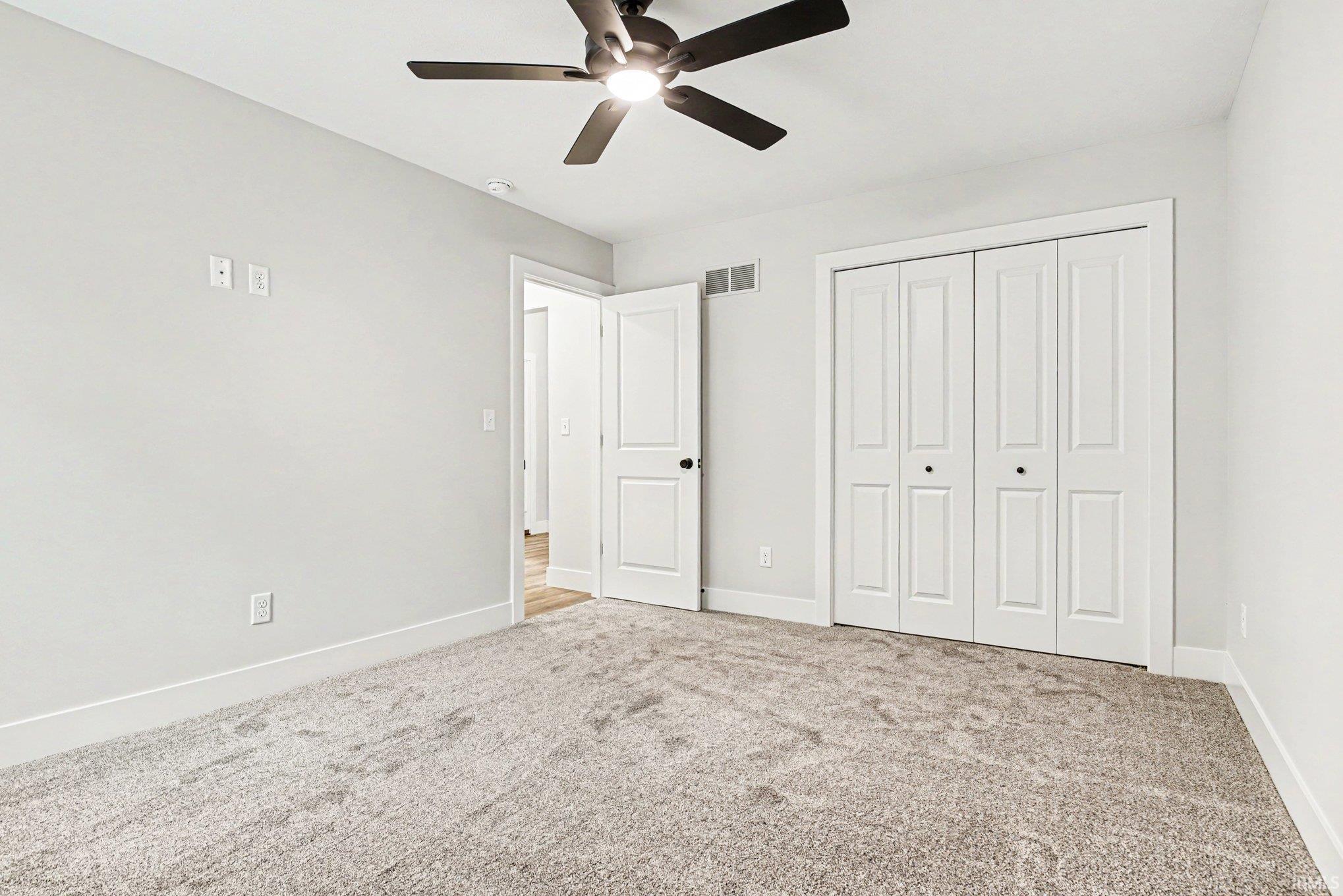 Spacious room featuring light gray carpeting, neutral wall color, white baseboards, a ceiling fan with integrated lighting, and bi-fold closet doors