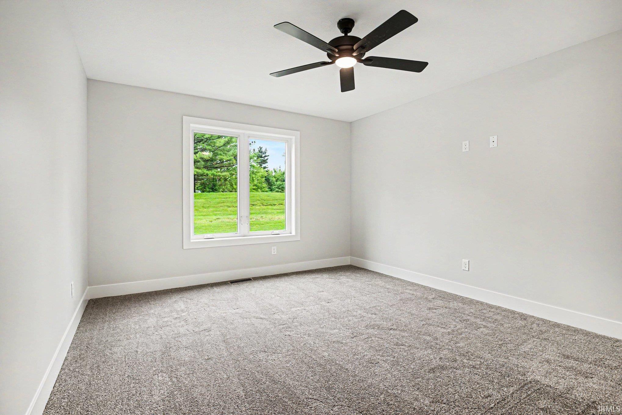 Bright room featuring a large window, neutral gray carpet, white baseboards, and a black ceiling fan with integrated lighting