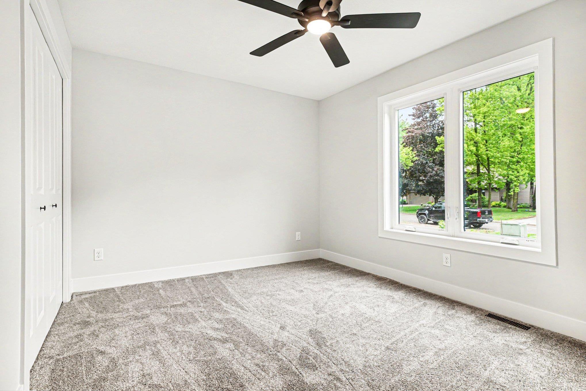 Bright room with a large window, plush gray carpet, and a modern ceiling fan