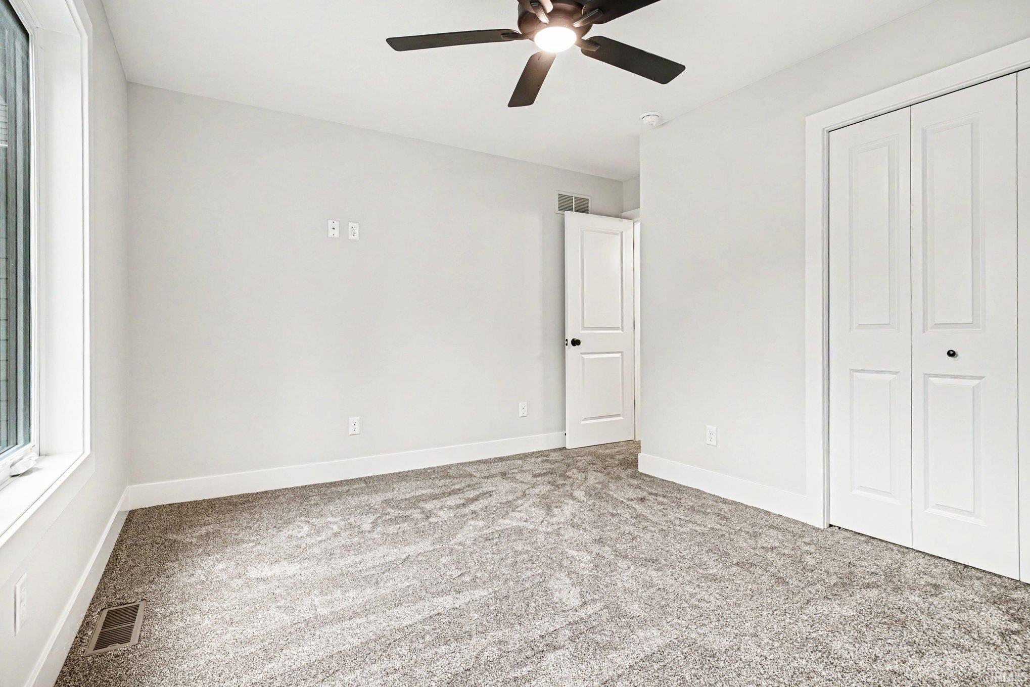 Carpeted room with a ceiling fan, a window, and white bi-fold closet doors