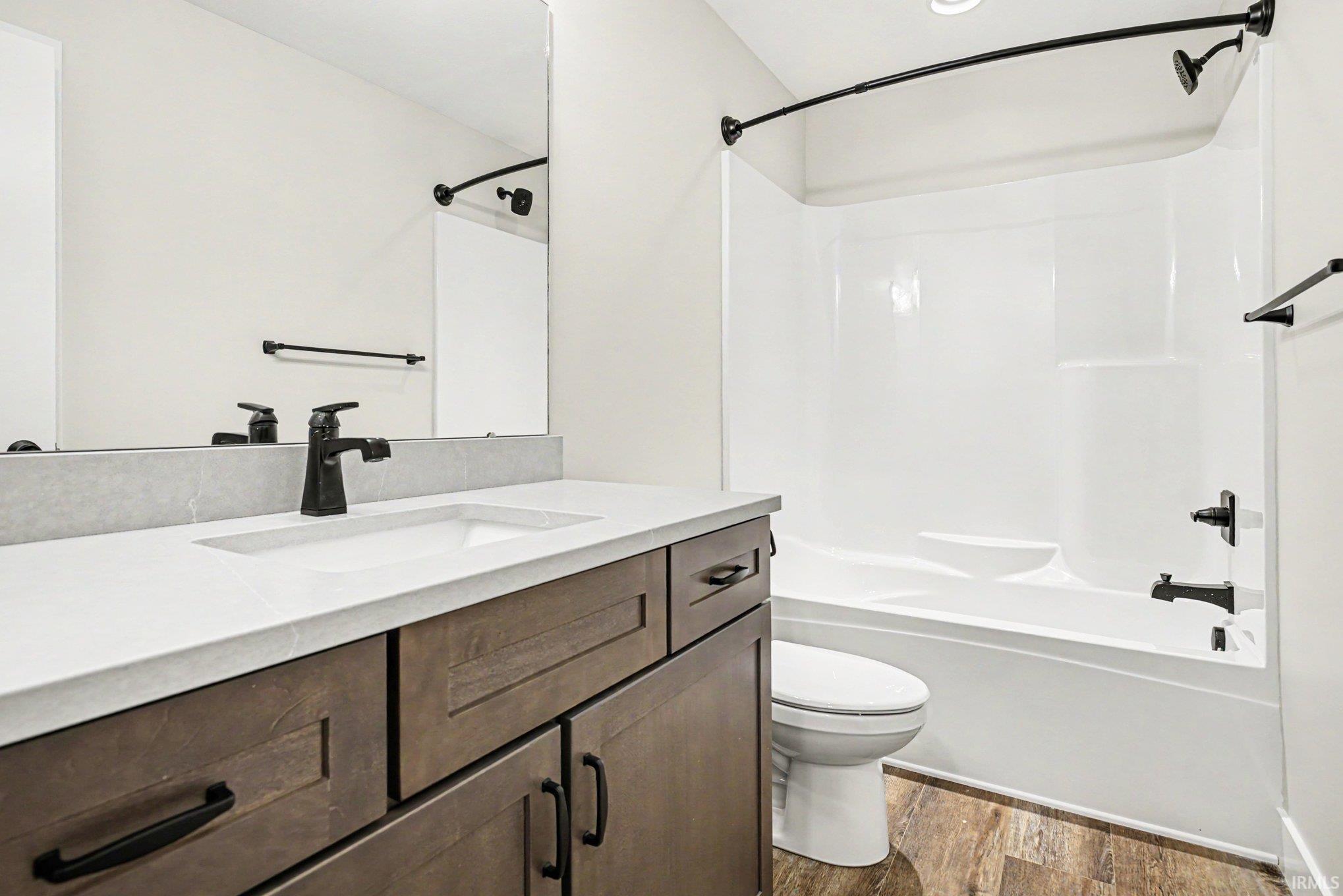 Bathroom featuring a wood-finish vanity with a white countertop and integrated sink, a large mirror, a white bathtub with shower, and wood-look flooring