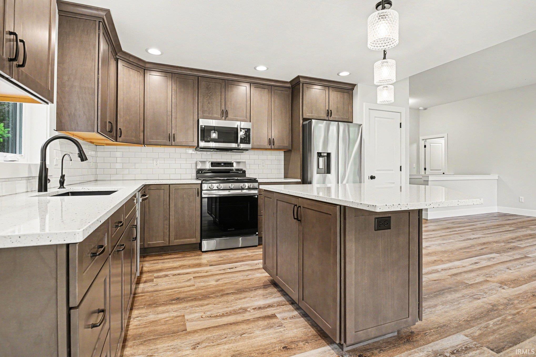 Modern kitchen featuring wood-finish cabinetry, light-toned countertops, subway tile backsplash, stainless steel appliances, and a central island with pendant lighting