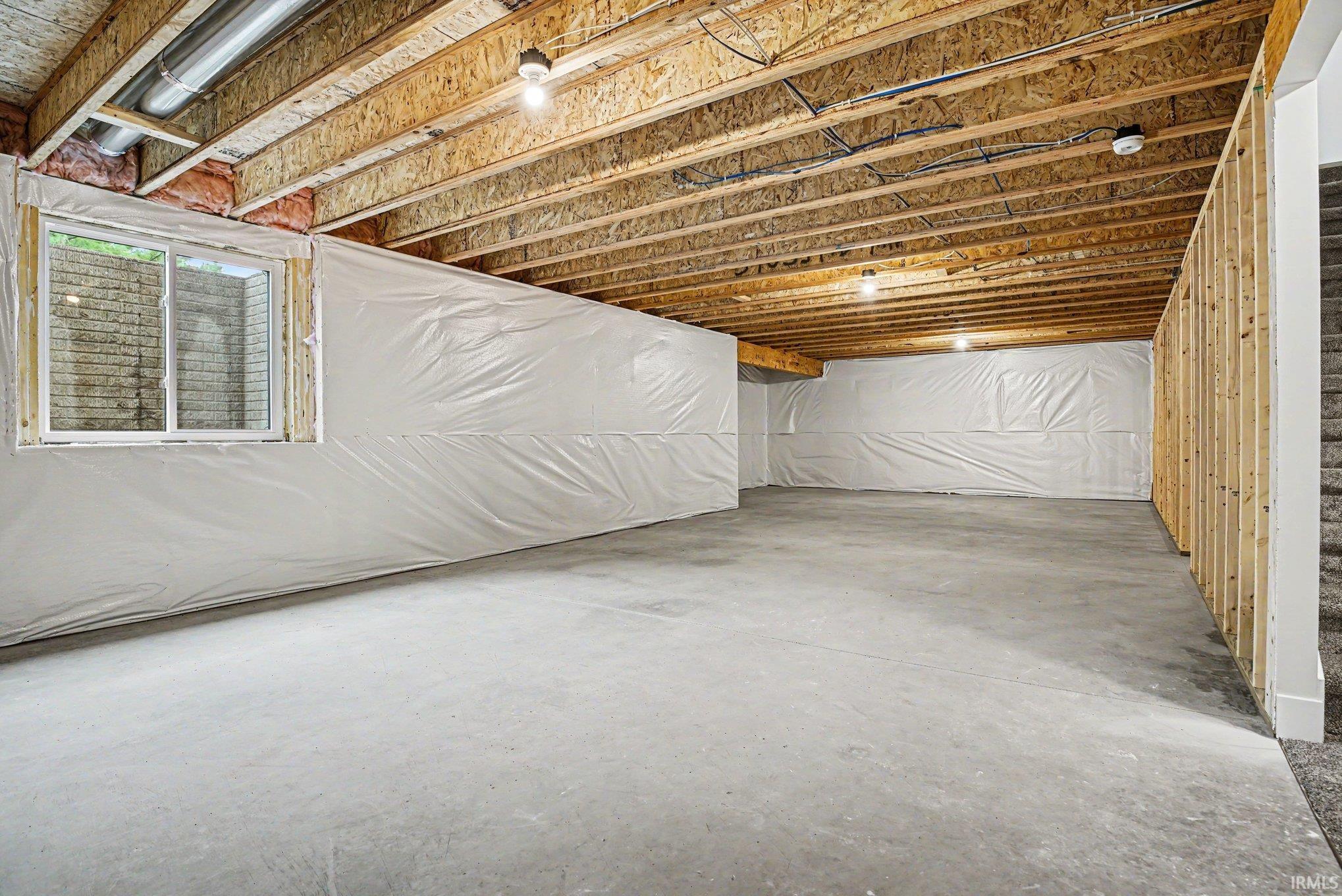 Unfinished basement featuring exposed wood joists, concrete flooring, and a single window
