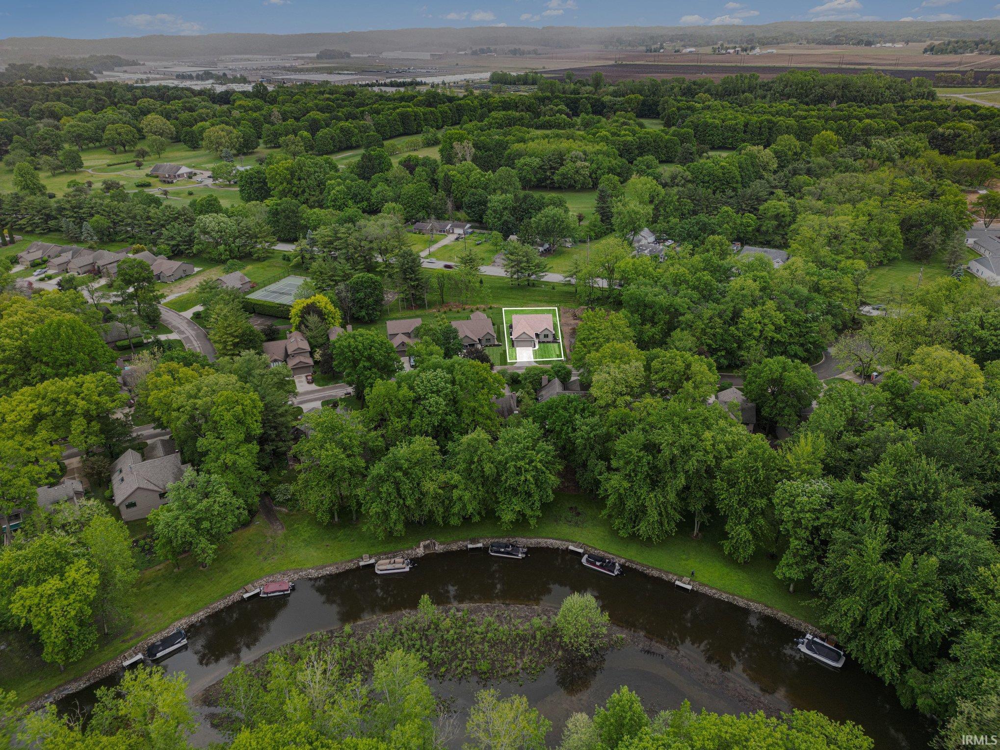 Aerial perspective showcasing a property surrounded by mature trees, highlighting its proximity to a body of water with docked boats