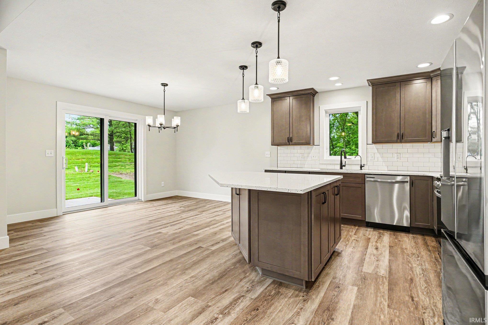 Contemporary kitchen featuring wood-finish flooring, a central island with a light-toned countertop, and dark wood cabinetry
