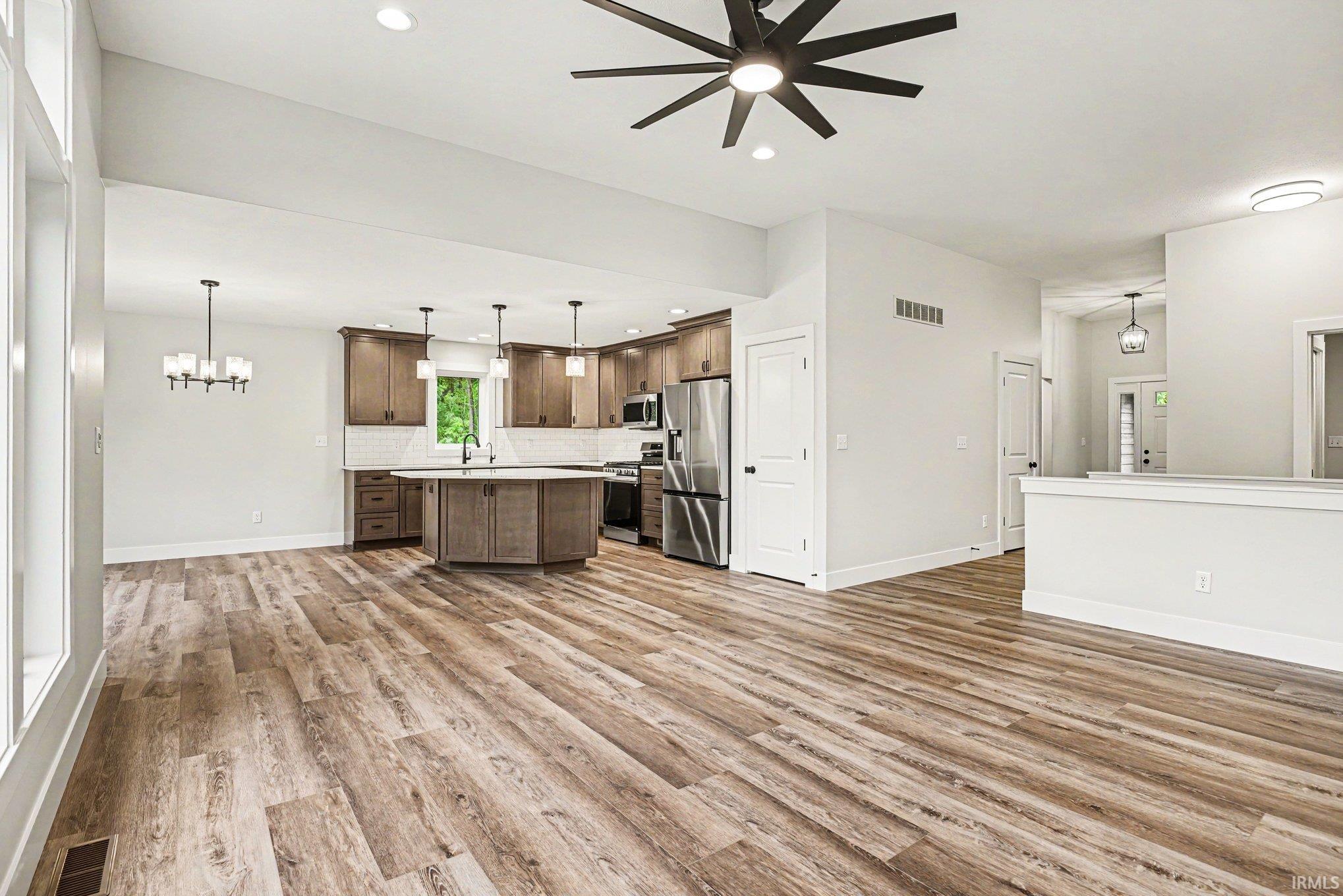 Open-concept living space featuring wood-finish flooring, a contemporary kitchen with stainless steel appliances, a kitchen island with pendant lighting, and abundant natural light from large windows