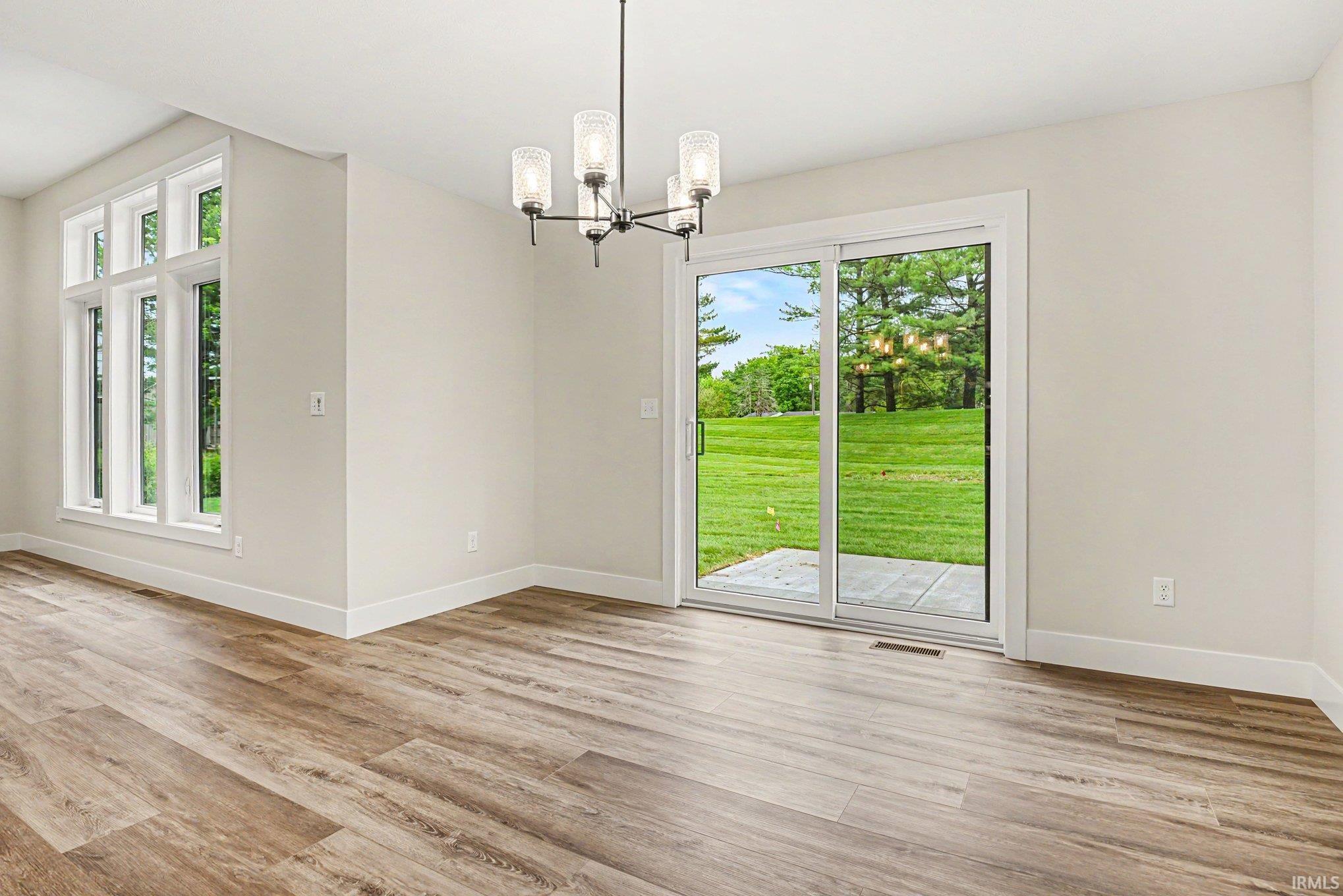 Spacious room featuring wood-finish flooring, a contemporary chandelier, large picture windows, and a sliding glass door leading to an outdoor patio with a manicured lawn