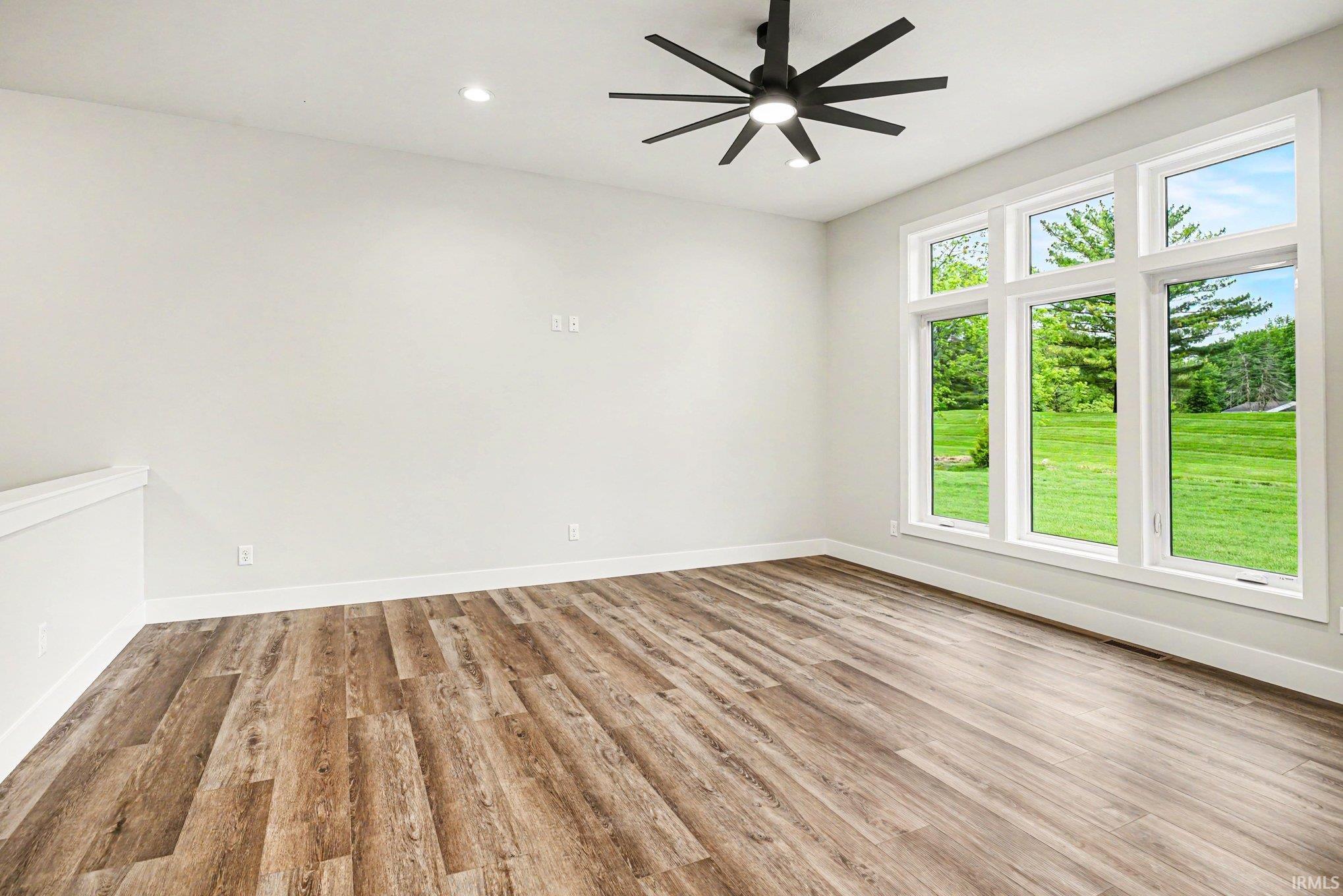 Open interior room featuring wood-finish flooring, white baseboards, and a modern ceiling fan with integrated lighting