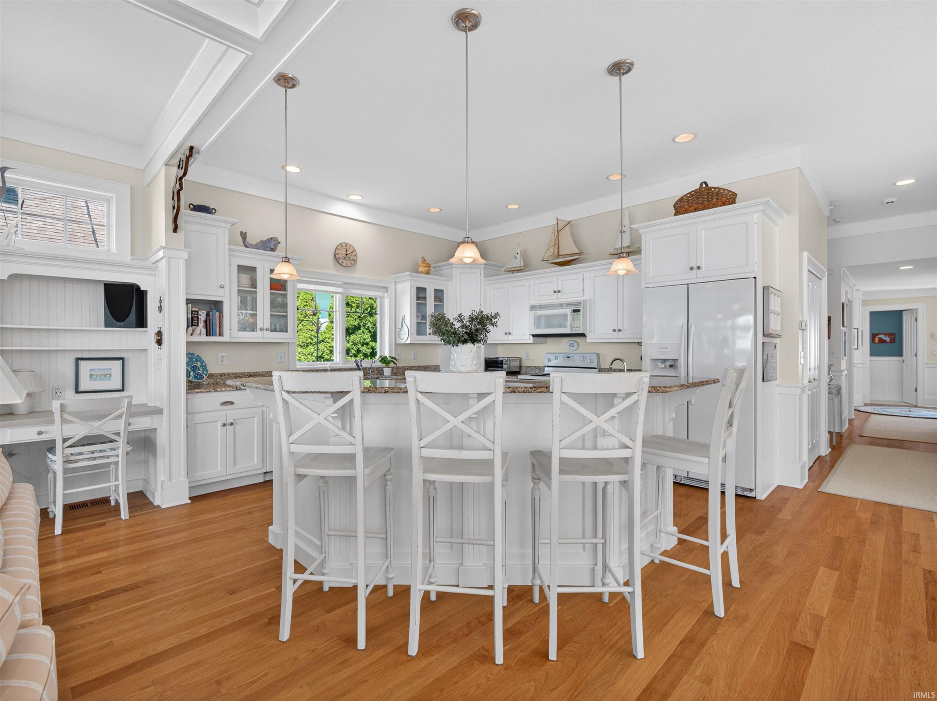 Open-concept kitchen featuring white cabinetry, a central island with bar seating, granite-finish countertops, wood-finish flooring, and recessed lighting