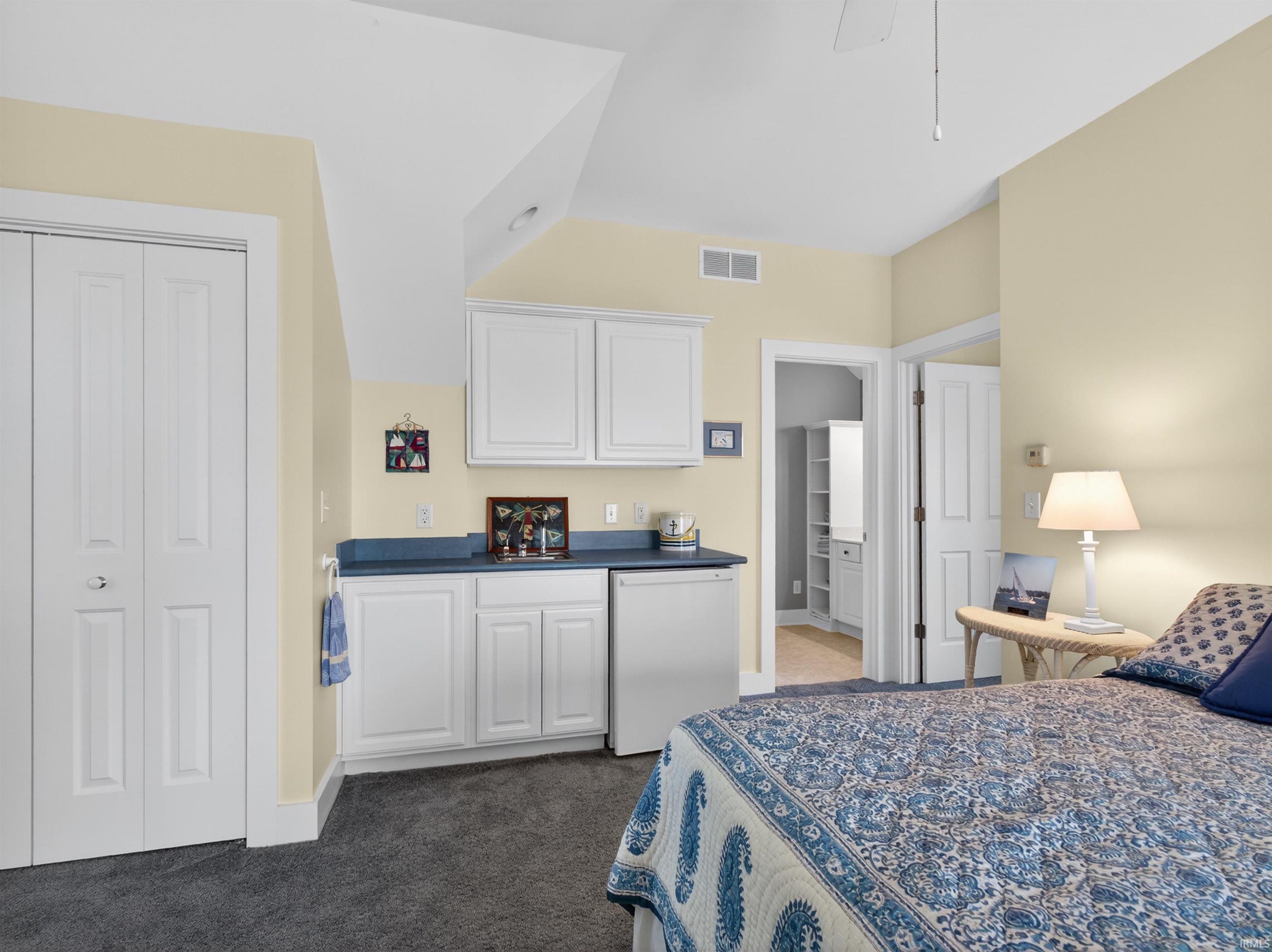 Bedroom featuring a built-in wet bar with white cabinetry, a blue countertop, and a stainless steel compact refrigerator