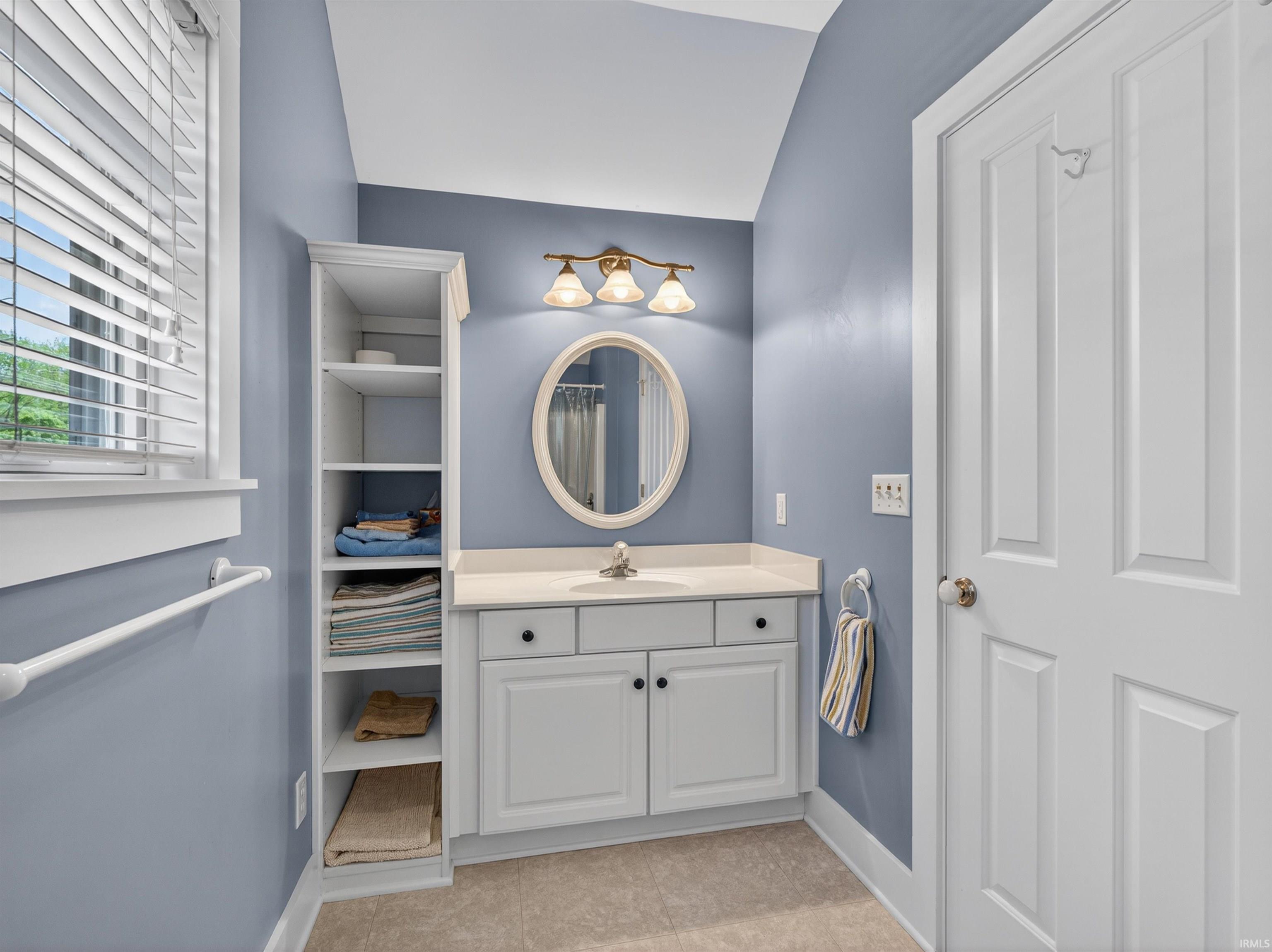 Bathroom vanity featuring a light-colored countertop, white cabinetry with black hardware, and an oval mirror with an ornate frame