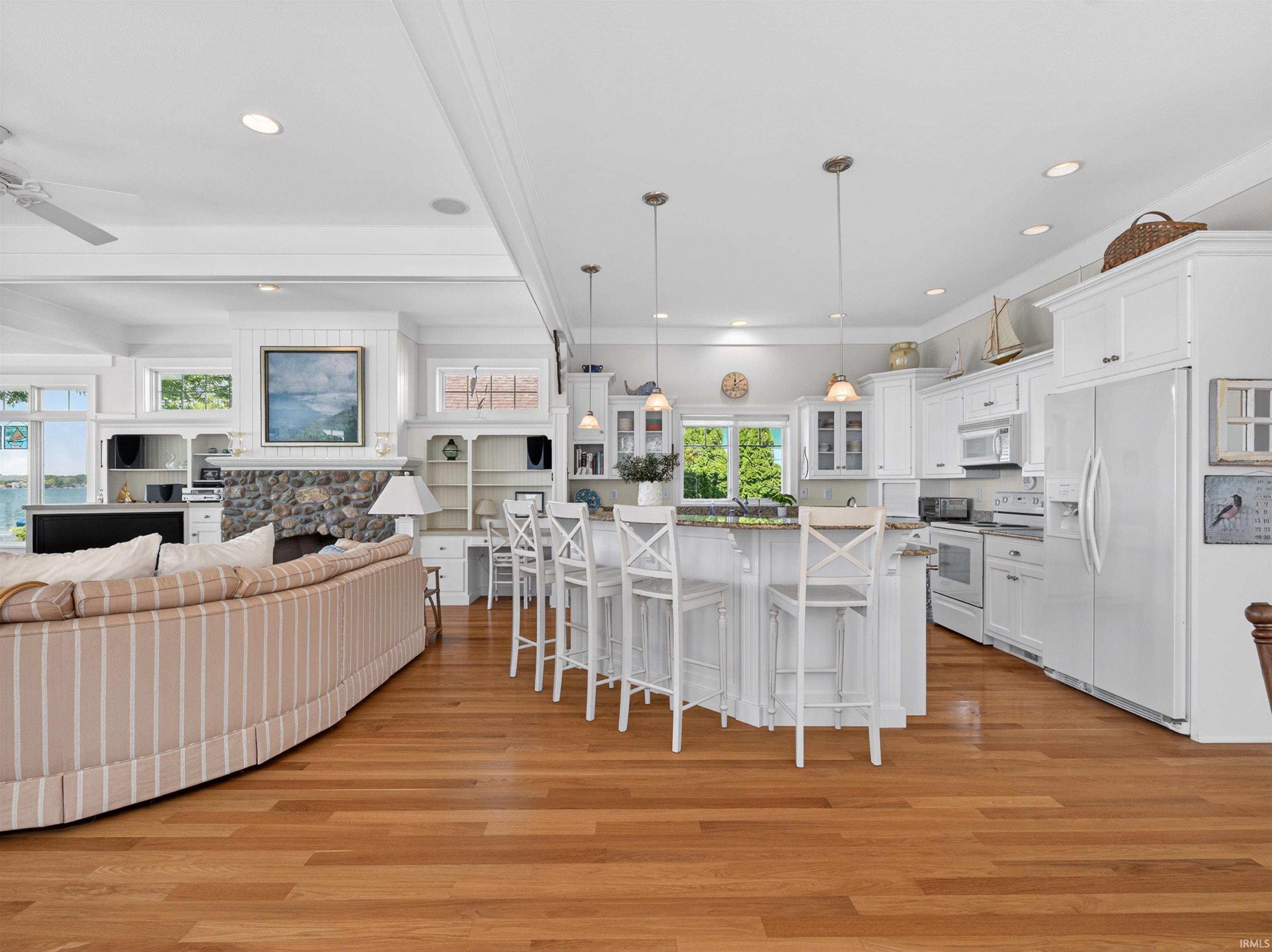 Open-concept living space featuring wood-finish flooring, a stone-faced fireplace, recessed lighting, and white cabinetry