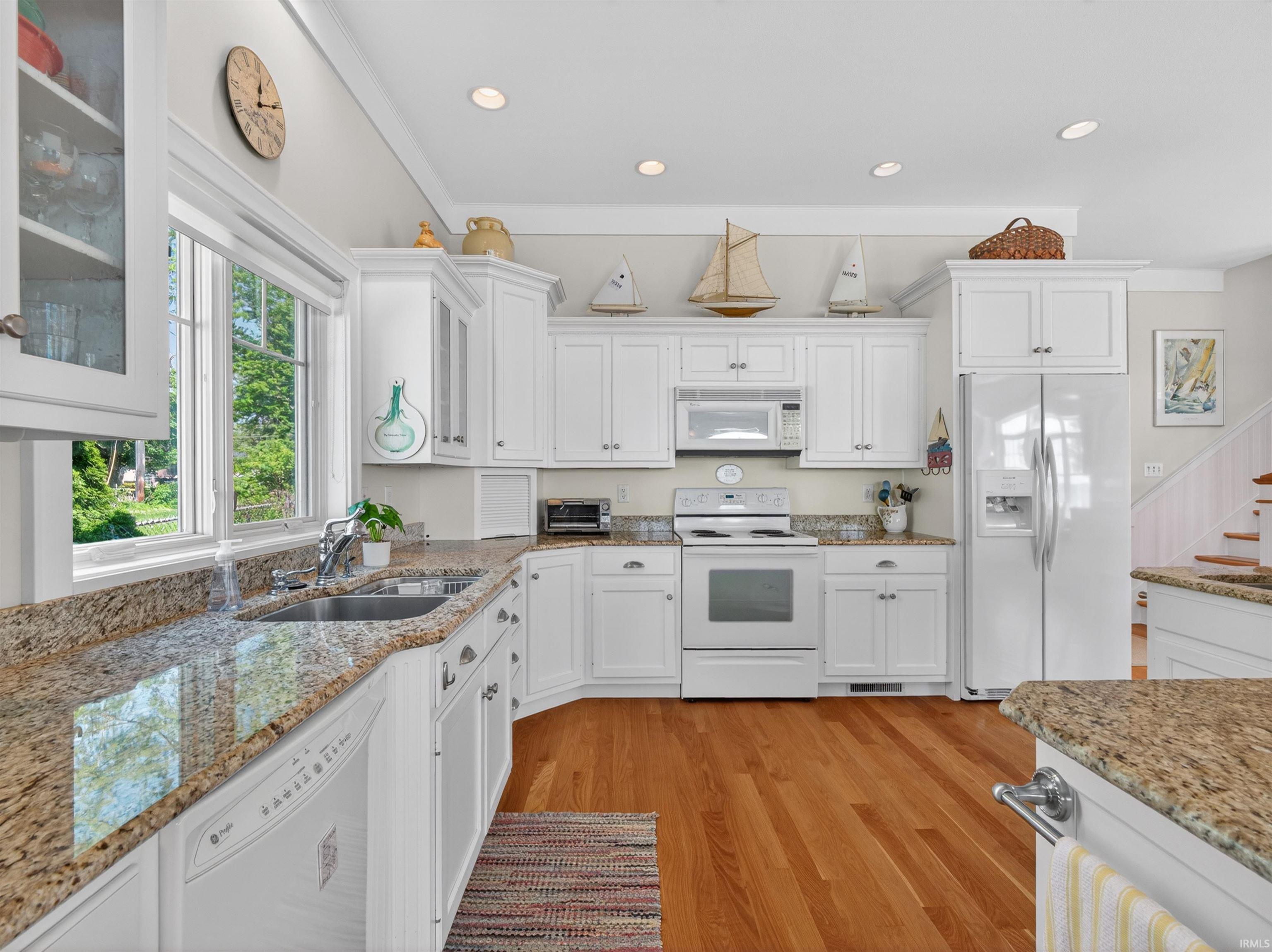 Bright kitchen featuring white cabinetry, granite countertops, stainless steel sink, a white range, and wood-finish flooring
