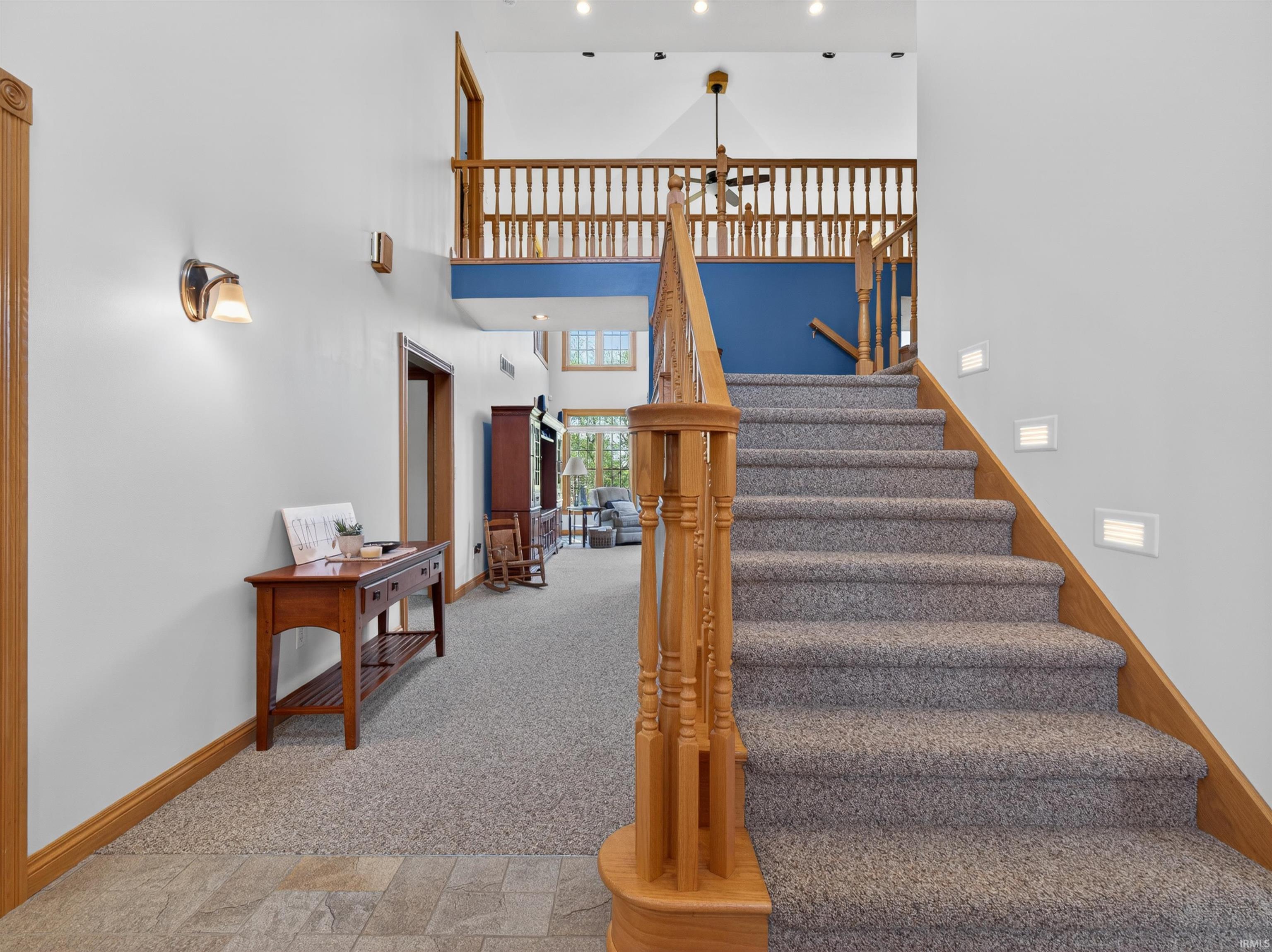 Grand entryway featuring a carpeted staircase with wood railings and integrated step lighting