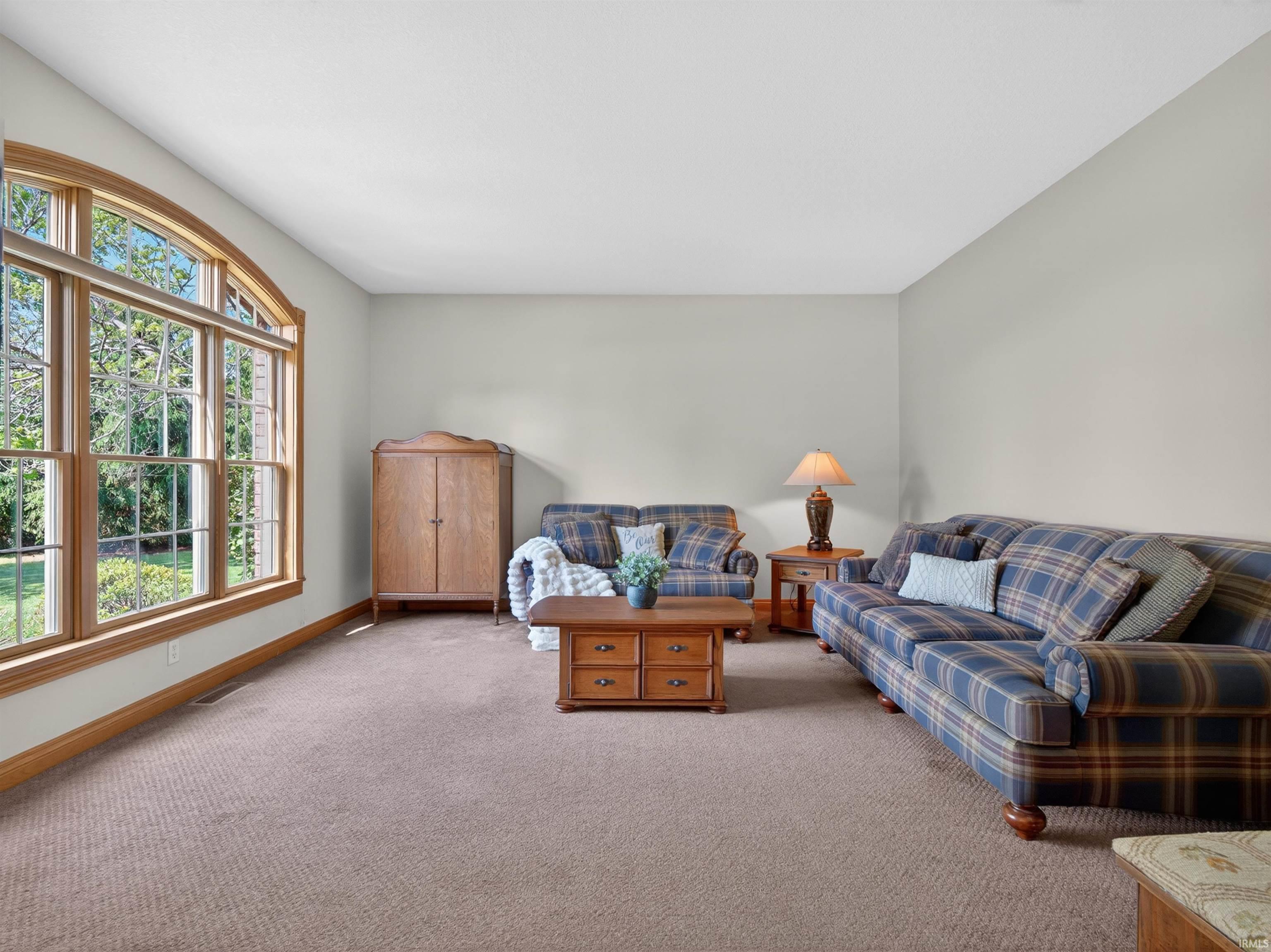 Spacious living area featuring an arched window, light-toned walls, and neutral carpeting