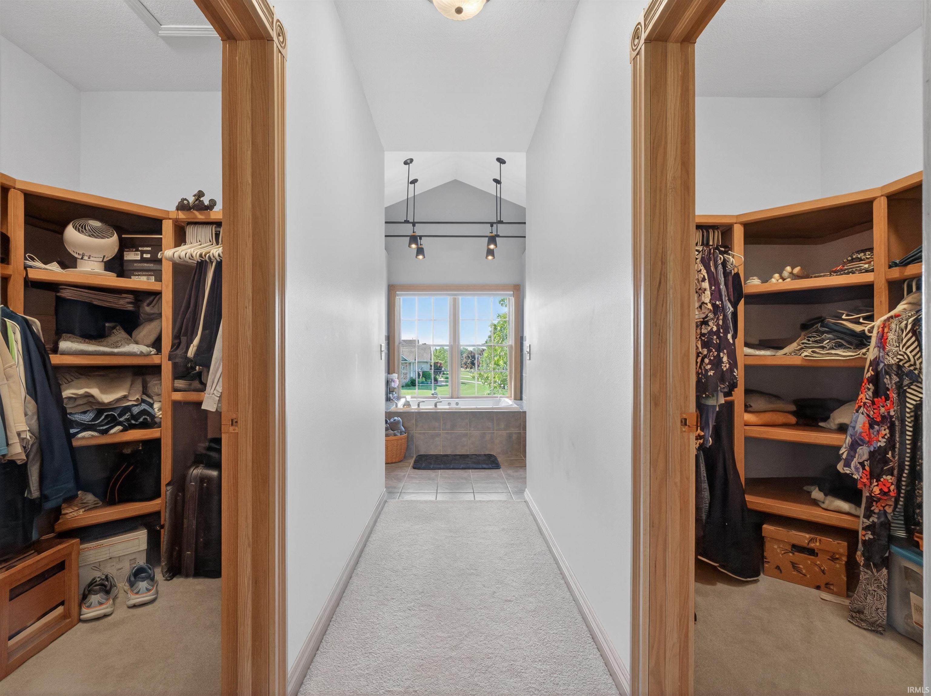 Carpeted hallway flanked by two walk-in closets with built-in wood shelving