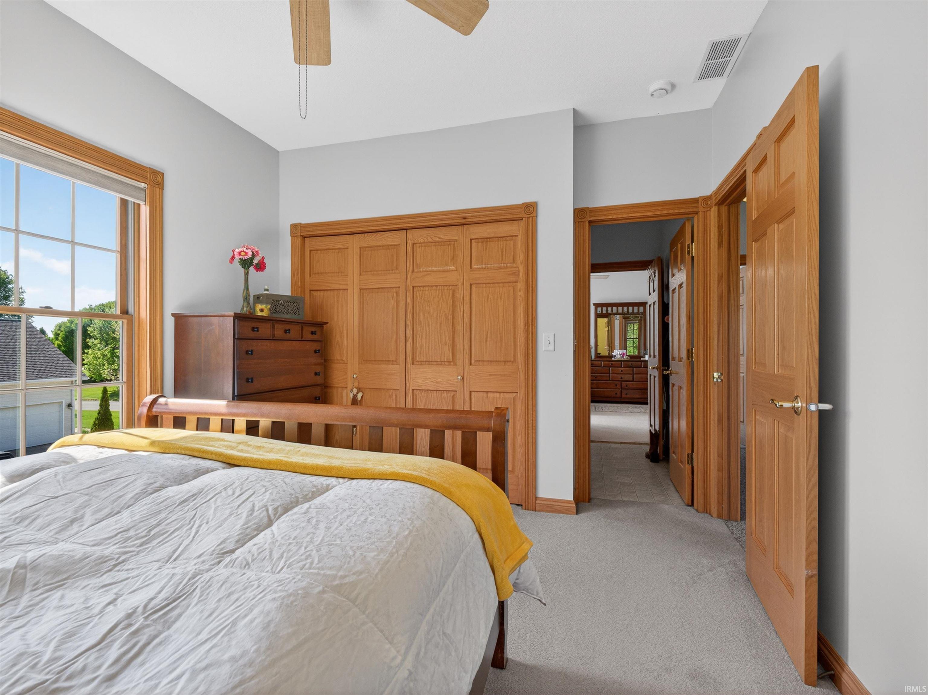 Carpeted bedroom featuring a large window with white muntins and wood trim, a ceiling fan with light fixture, and two panel wood doors